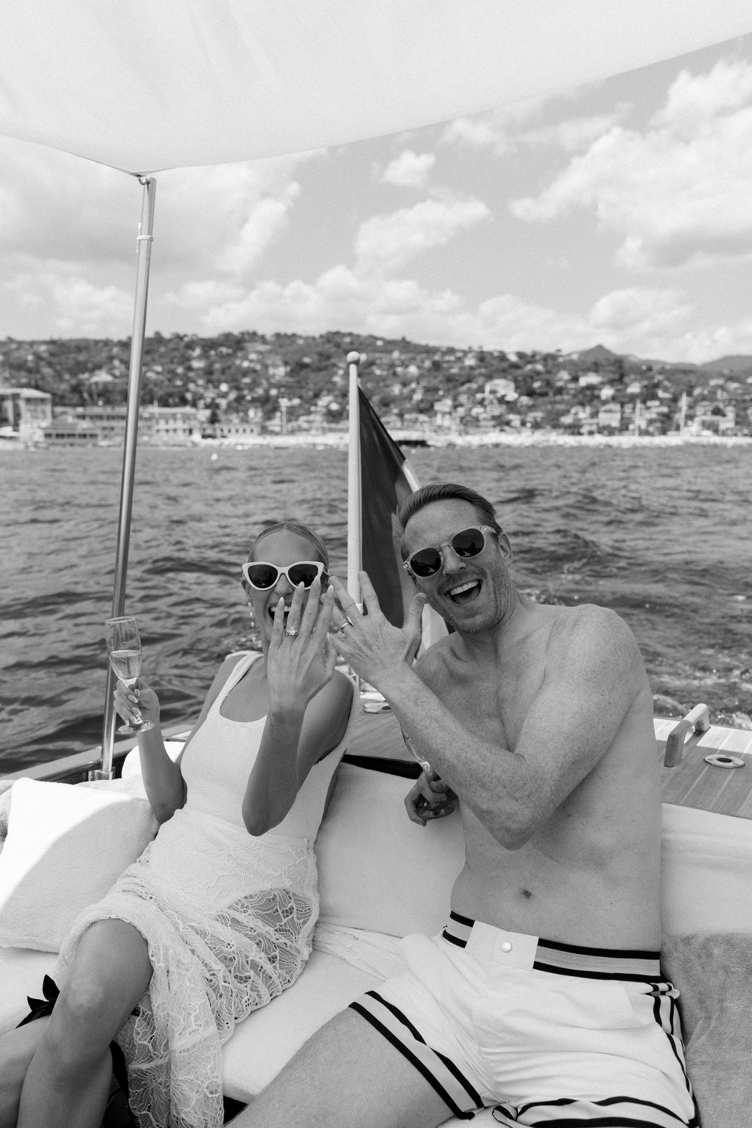 Joyful couple showing engagement ring on a boat with Italian coastal town in background.