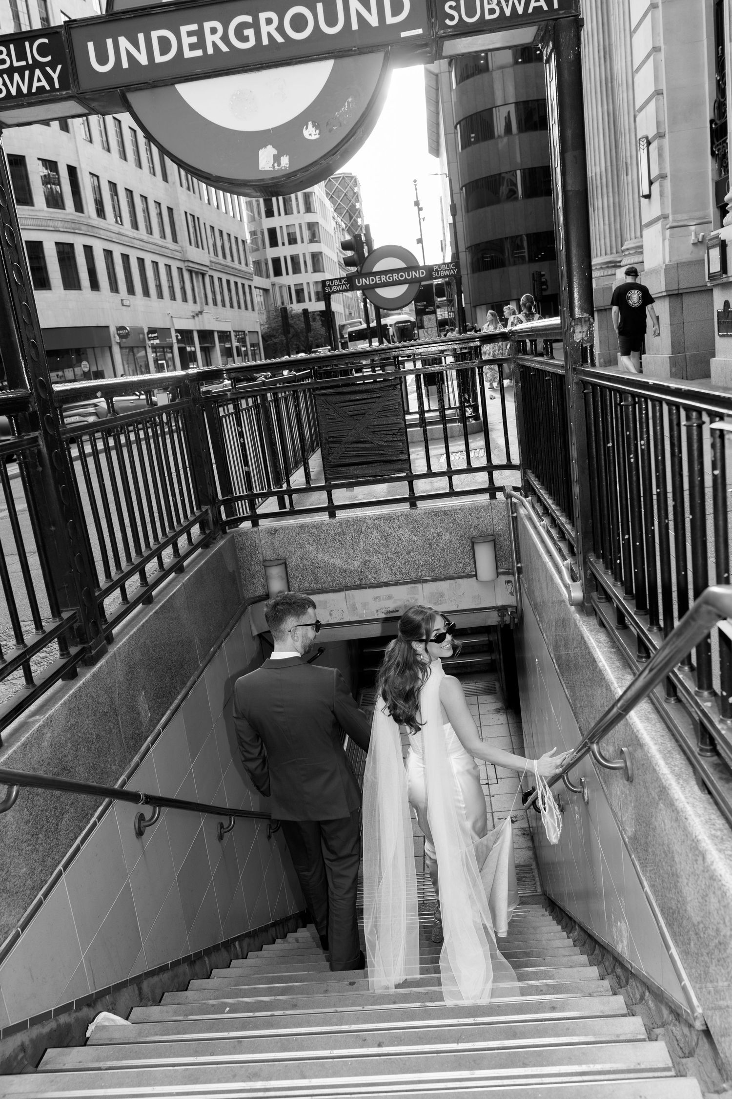 Black and white photo of bride and groom descending London Underground subway station stairs together.