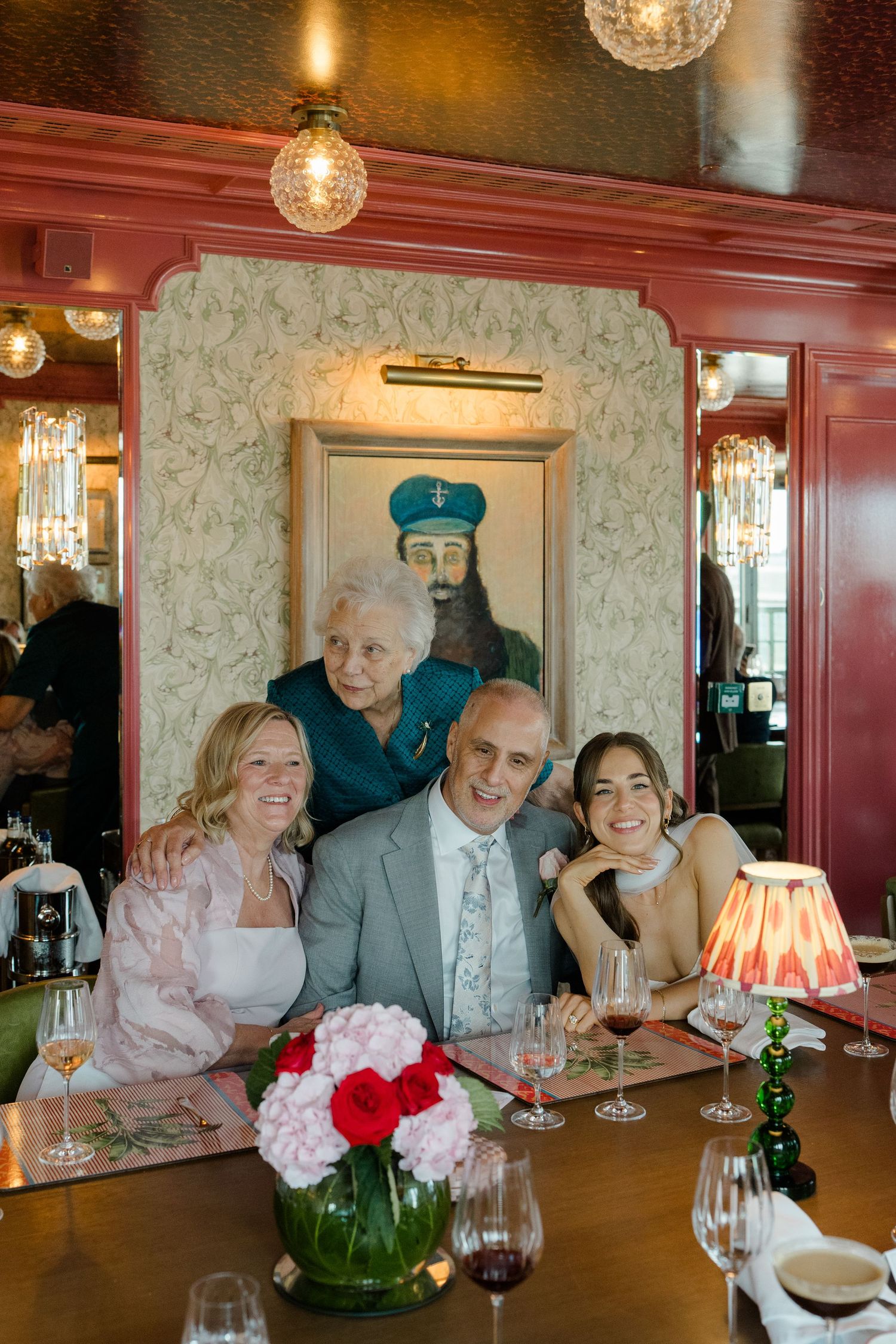 Family group smiles together at a decorated restaurant table beneath an ornate portrait painting.
