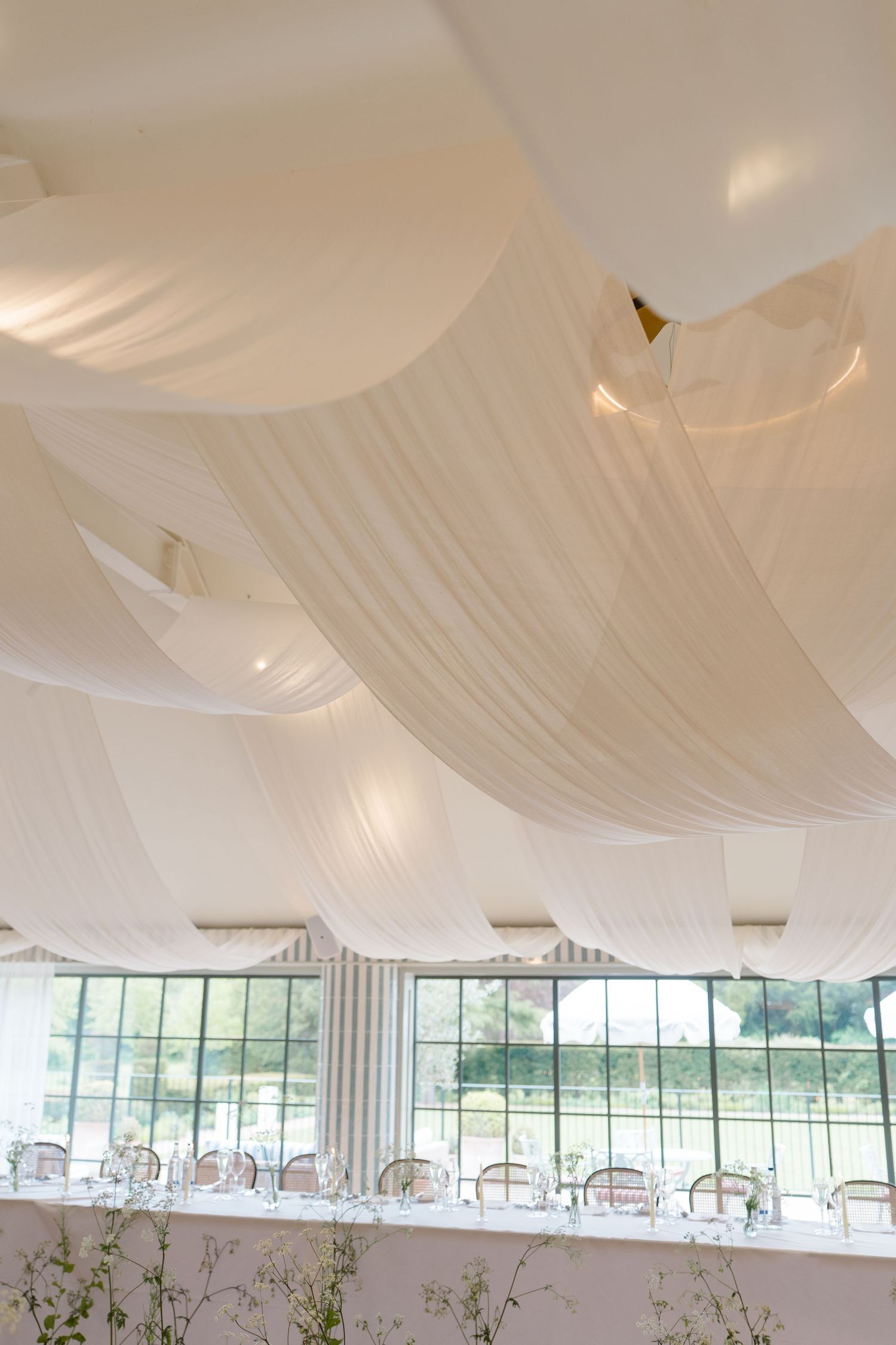 Elegant wedding reception venue with white draped ceiling fabric and long decorated tables.