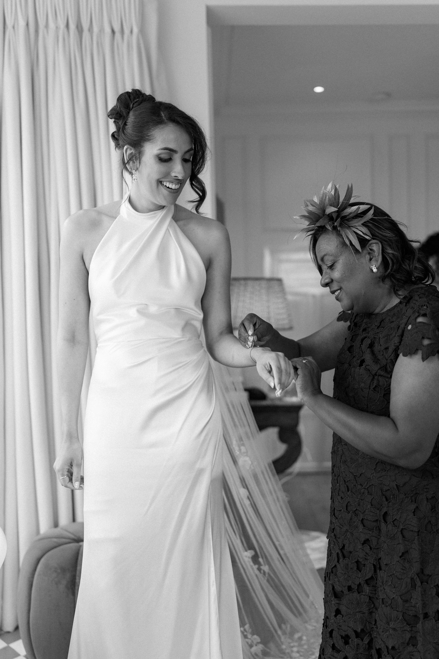 Bride in halter neck wedding gown smiling as guest sprays perfume on her wrist.