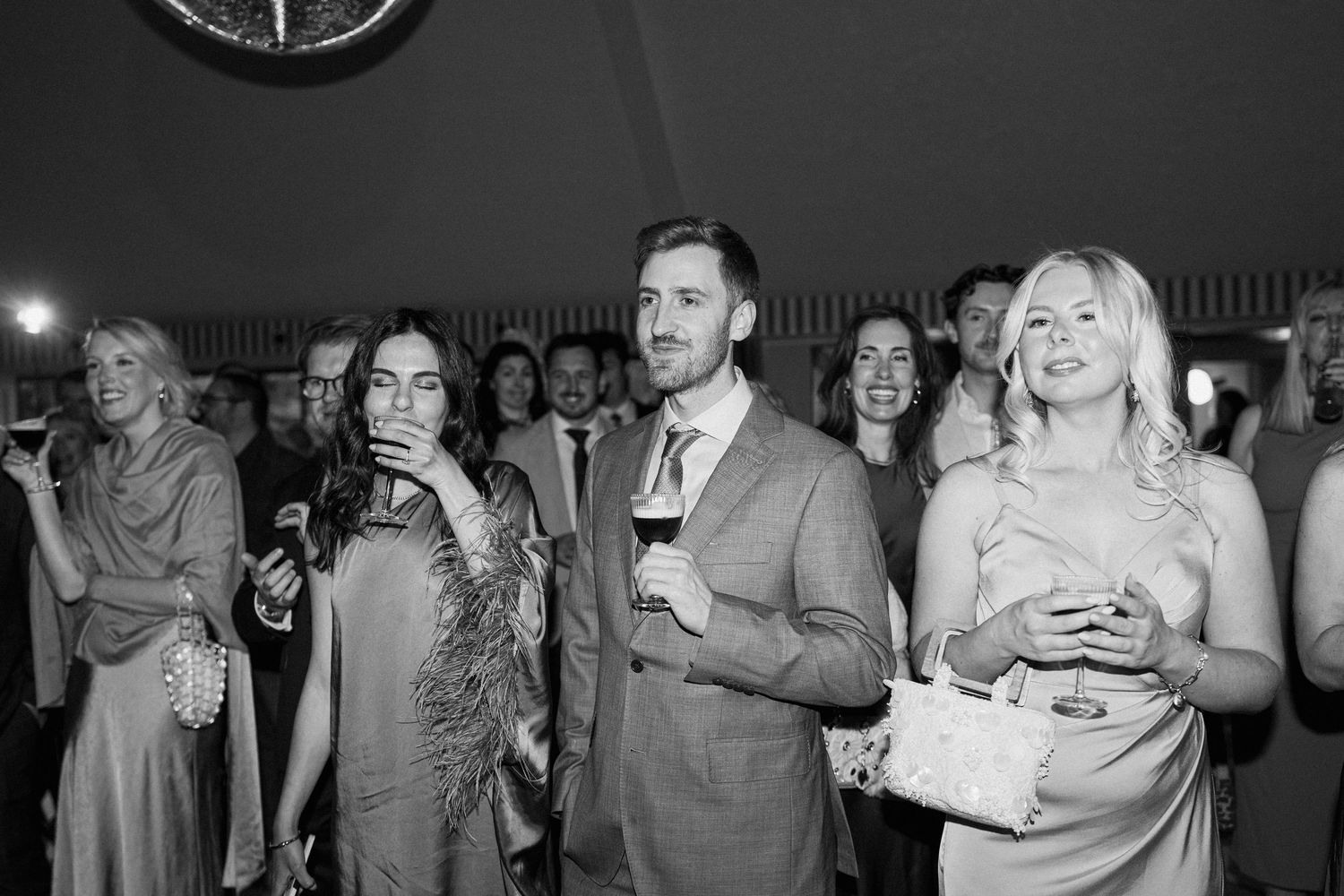 Wedding guests watch speeches attentively inside a marquee tent in black and white photo.