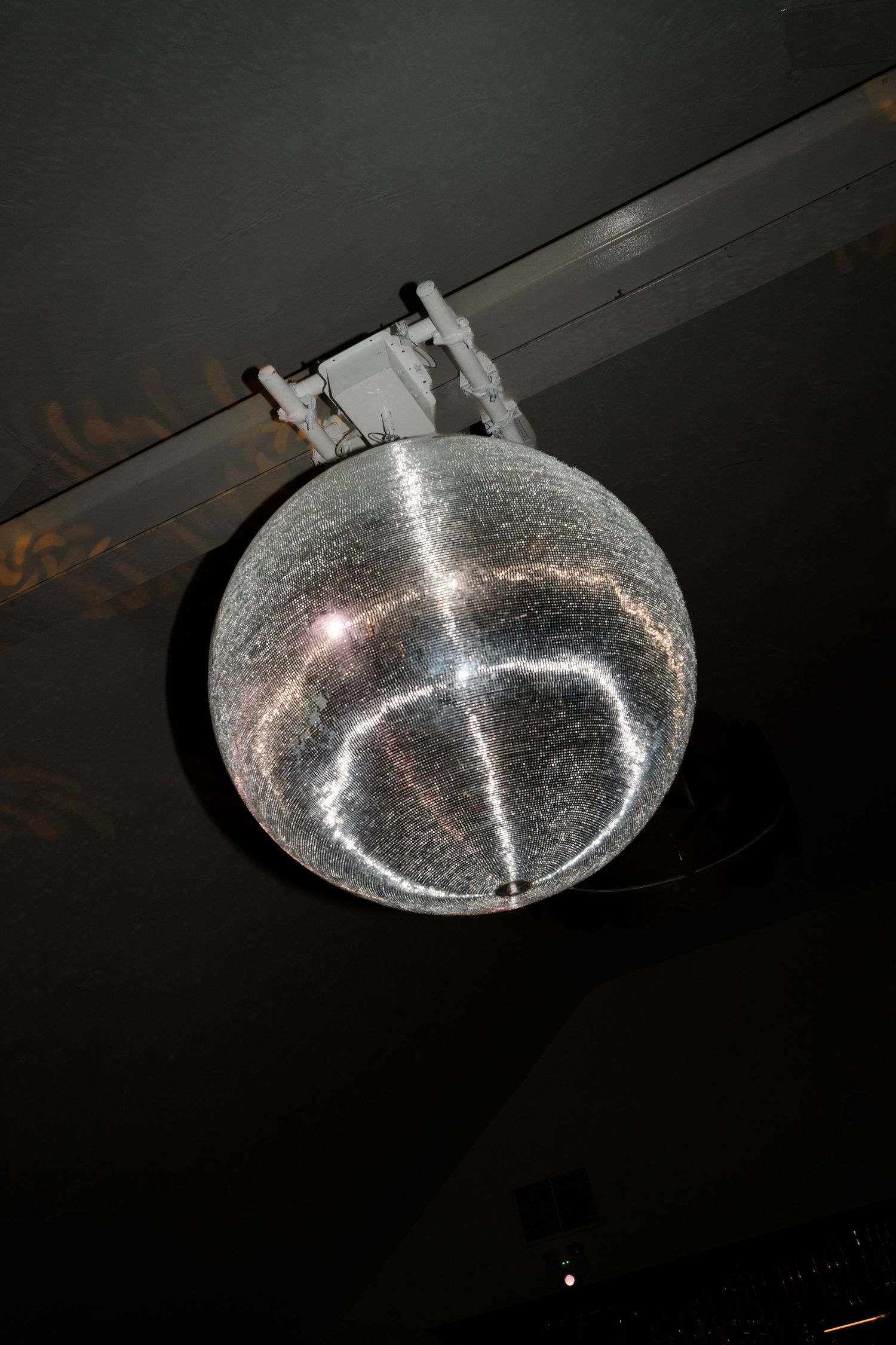 Sparkling disco mirror ball hanging from dark ceiling illuminated by bright light at wedding reception venue.