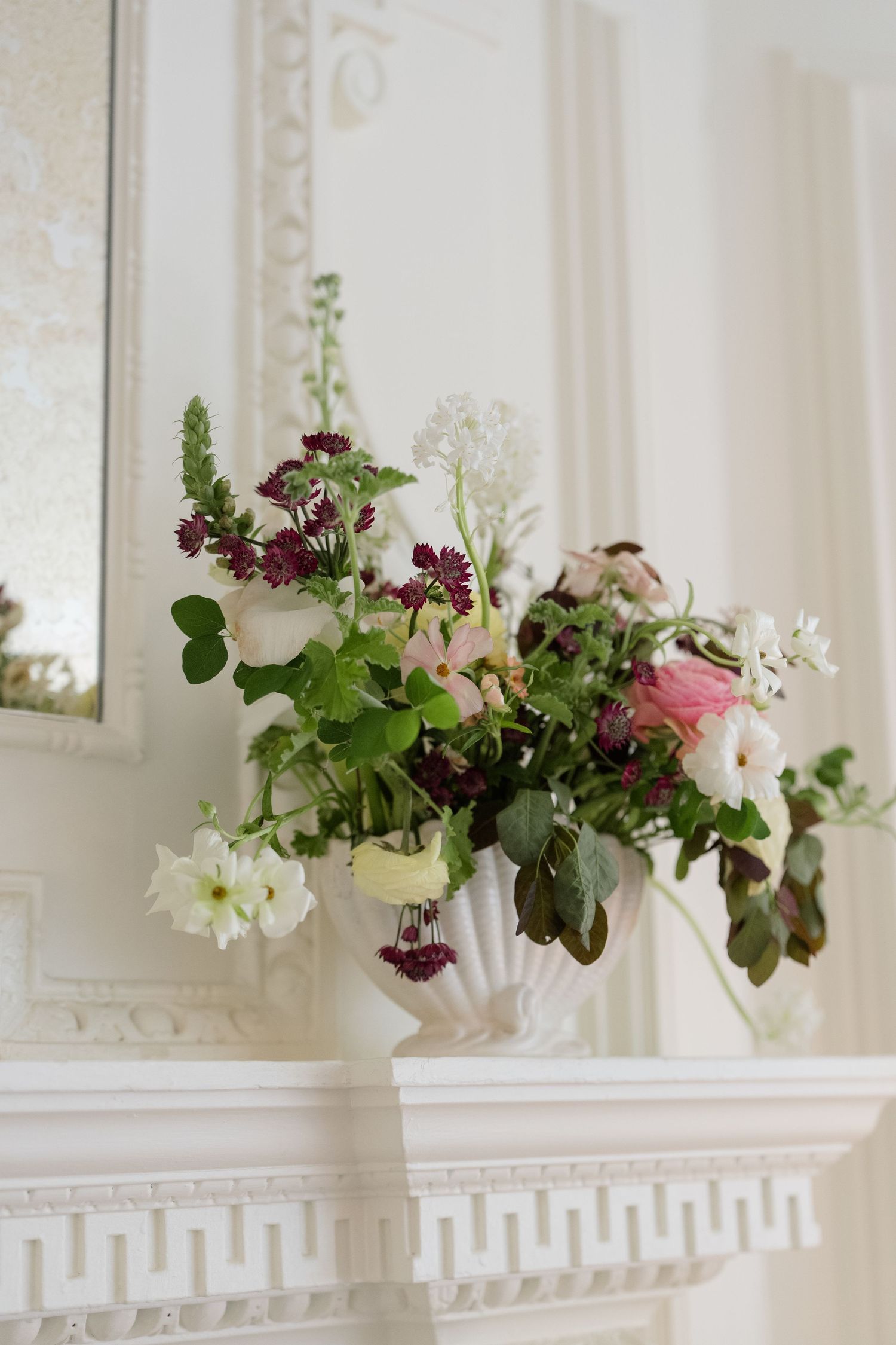 Elegant white floral arrangement with pink roses and burgundy blooms in a vase on a white fireplace mantel.
