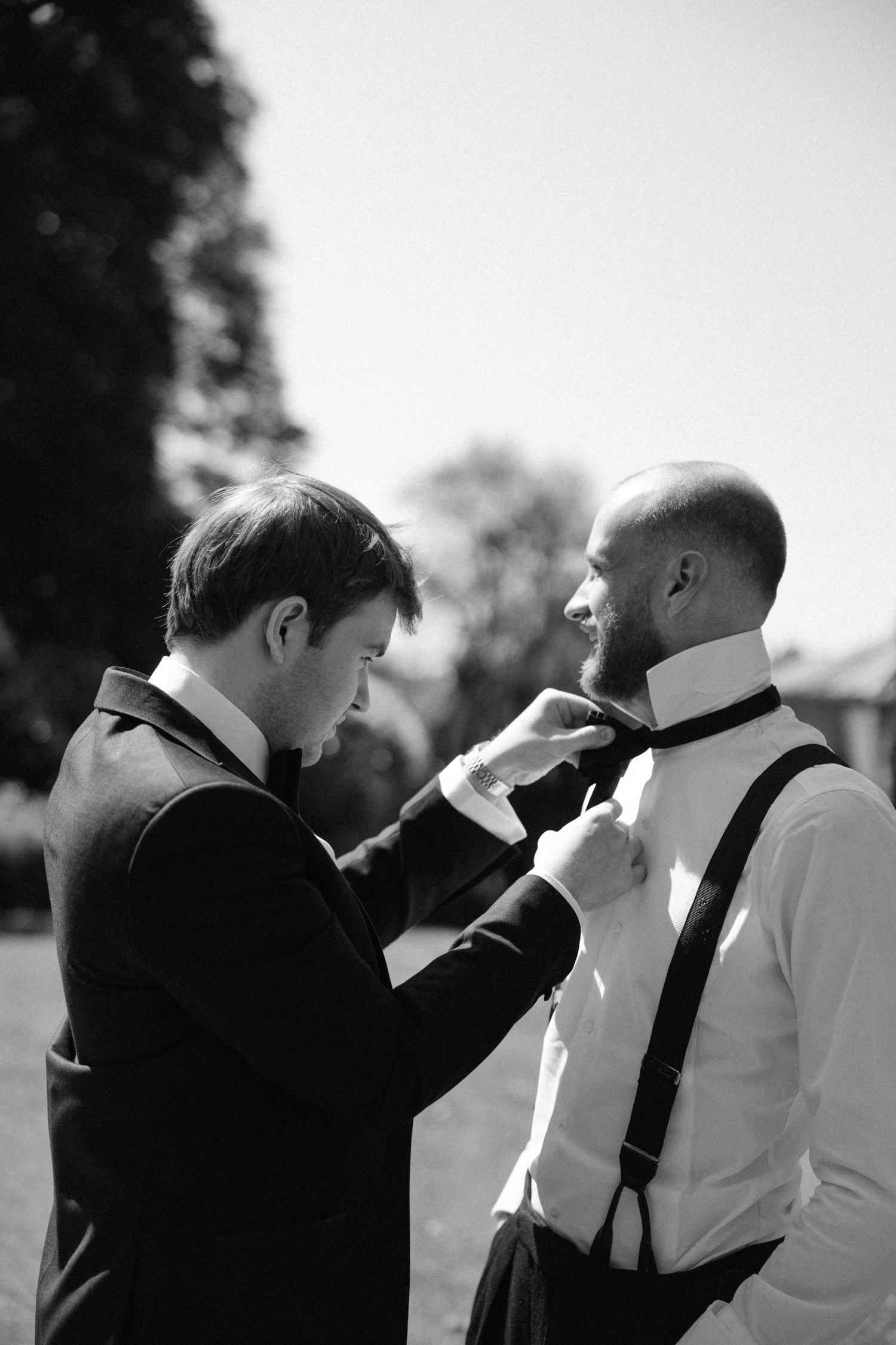 Groomsmen helping adjust ties and bowties before wedding ceremony in black and white.