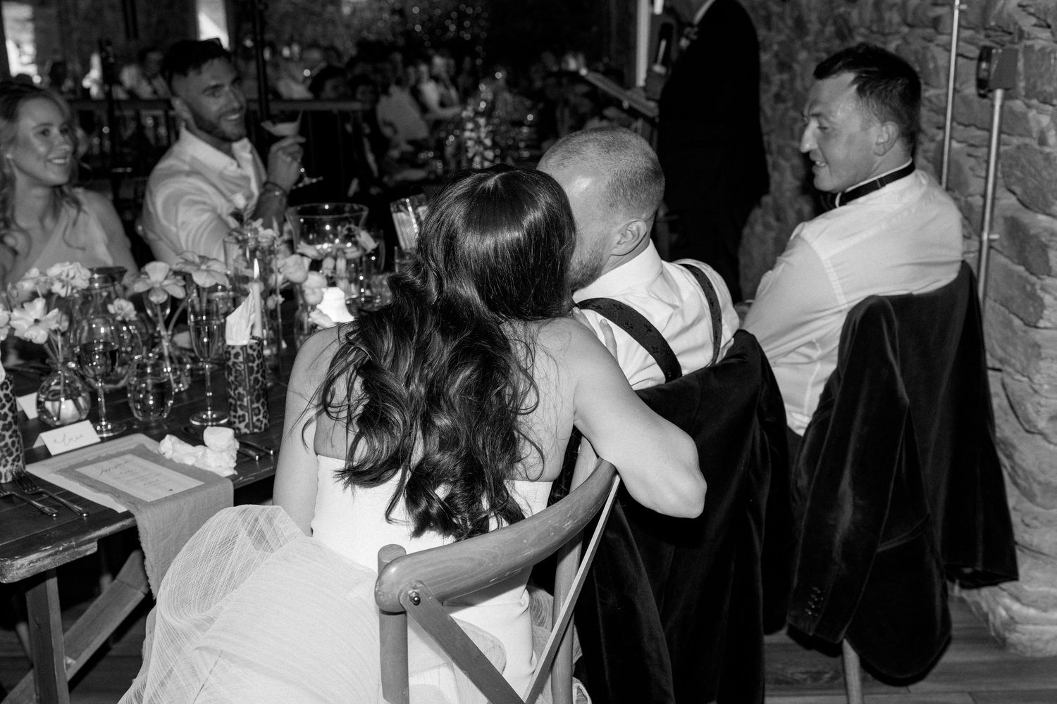 Wedding reception guests seated at decorated tables in rustic stone venue.