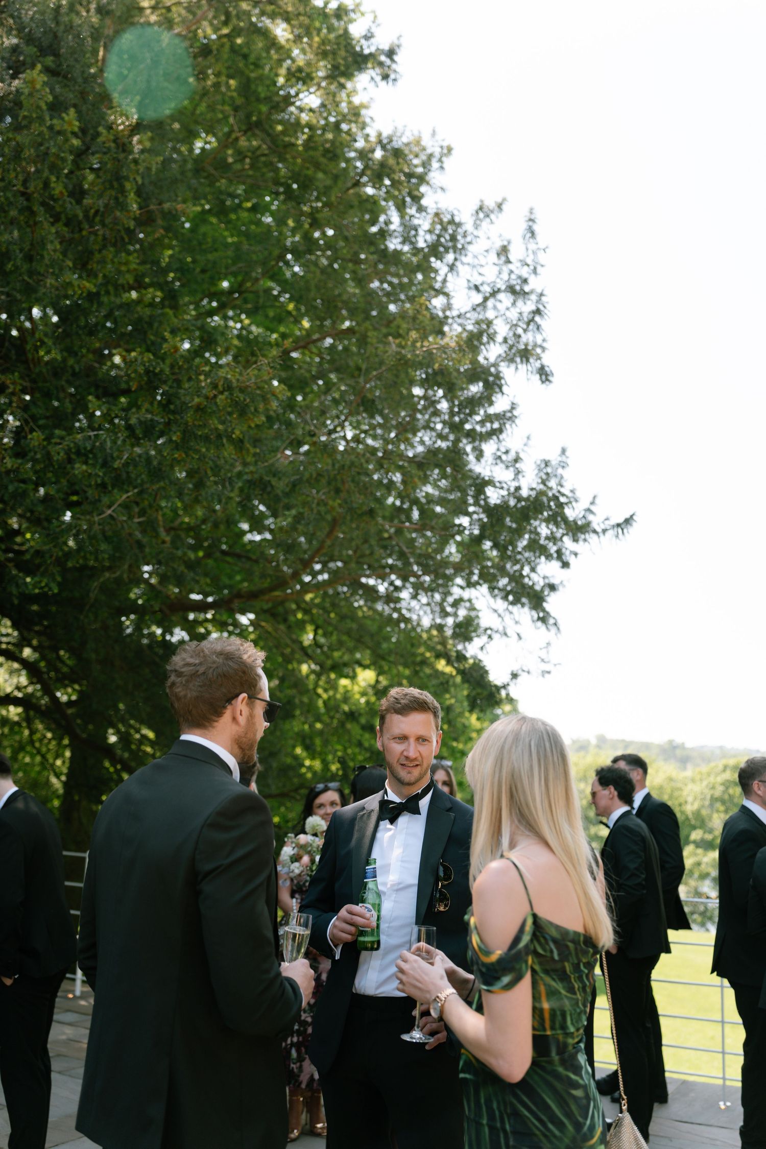 Guests in formal attire enjoying drinks during an outdoor cocktail reception.