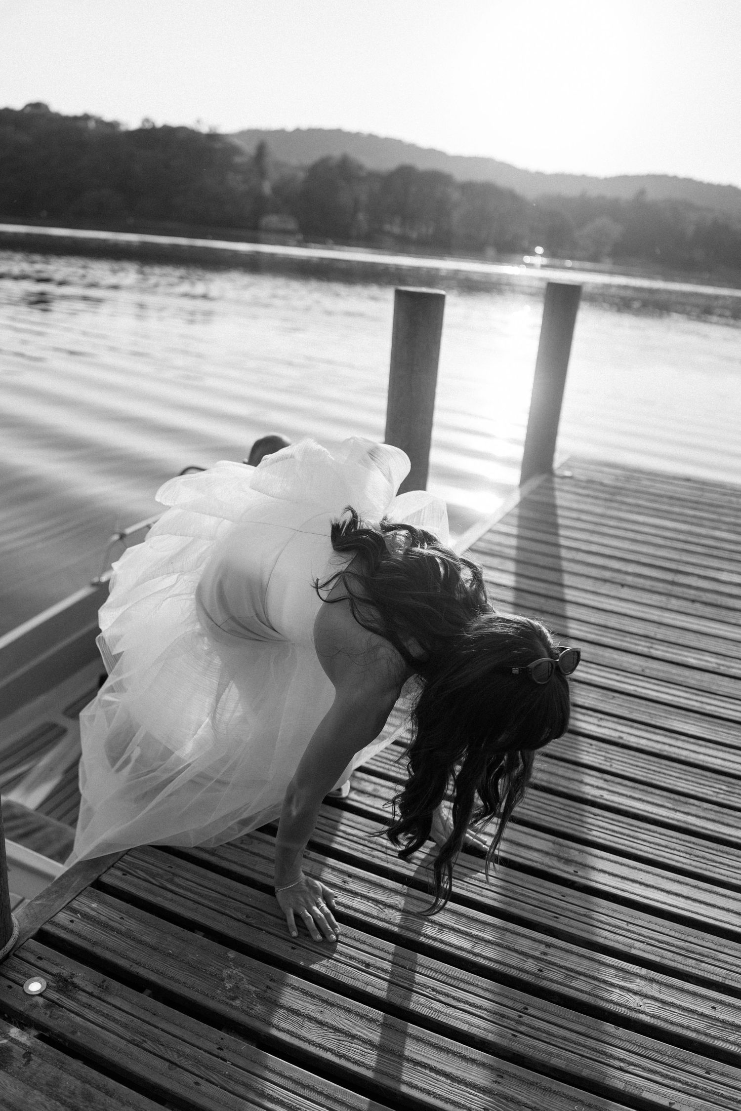 A couple in formal attire playfully posing on a wooden dock by the water.