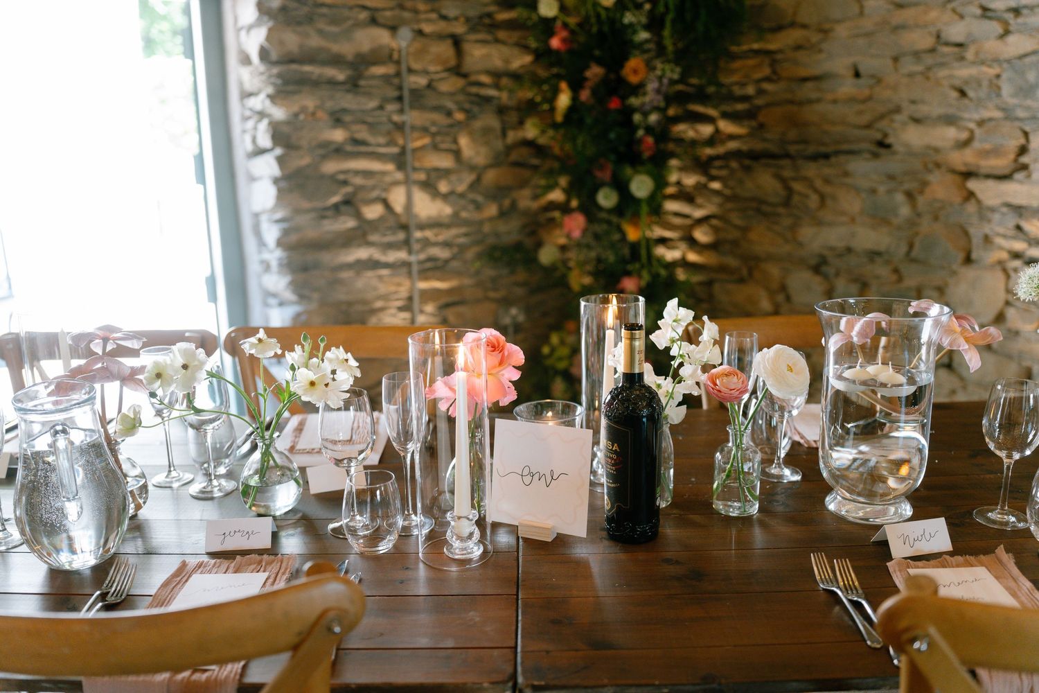 Rustic stone wall venue with elegant table settings and glassware arranged for a special event.