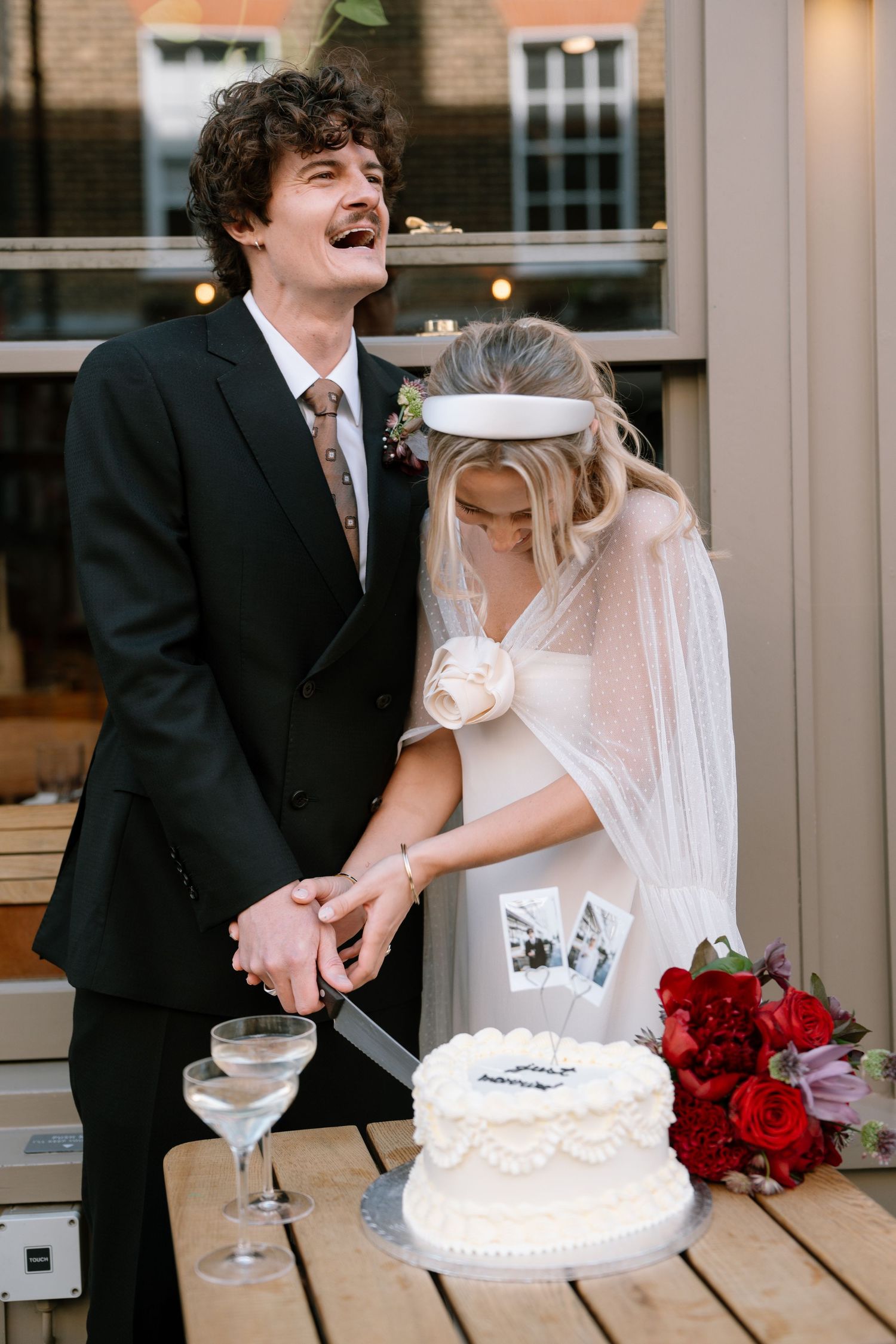 Newlyweds share a laugh while standing next to their wedding cake and champagne.