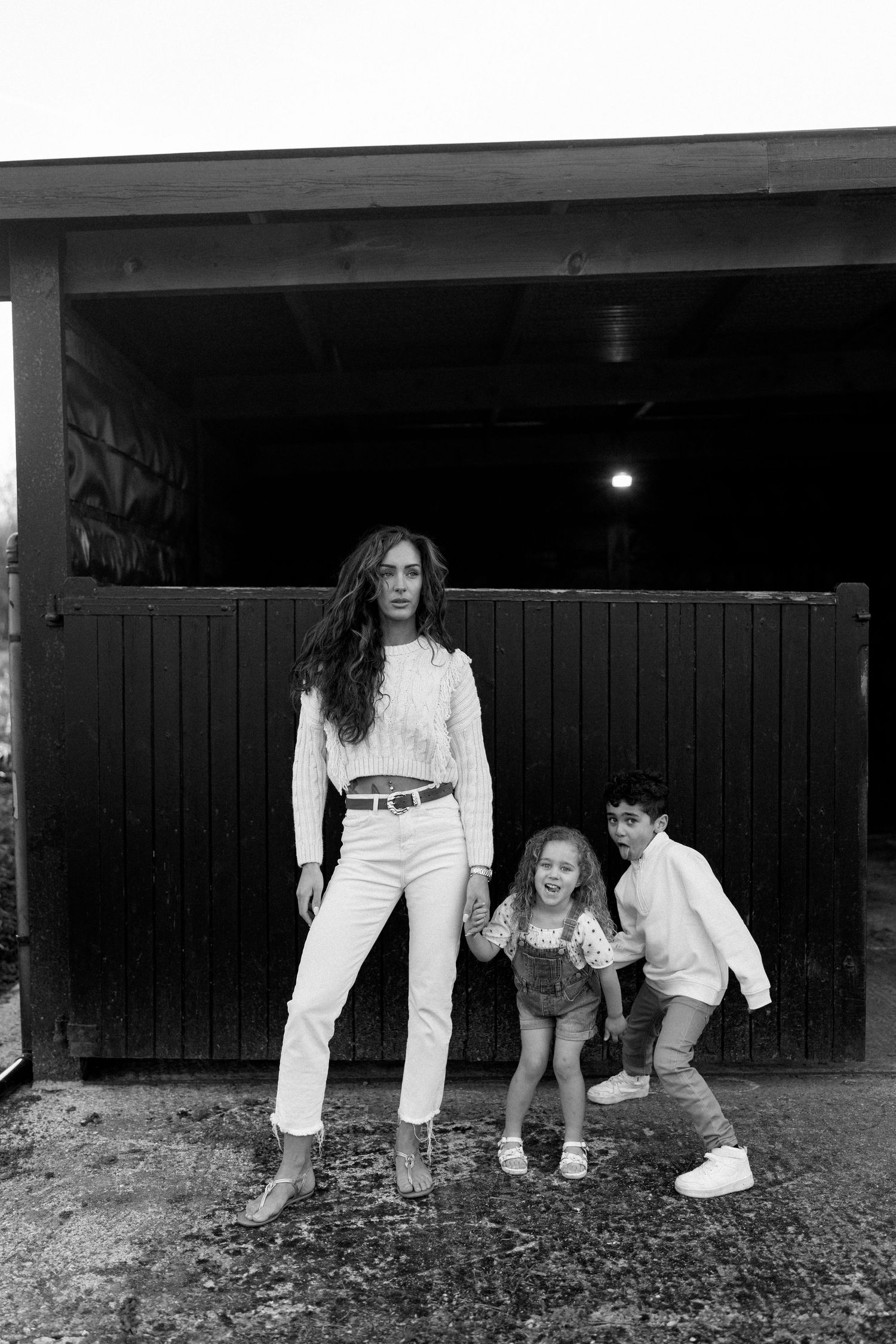 People in white clothing crawling playfully under a dark wooden structure.