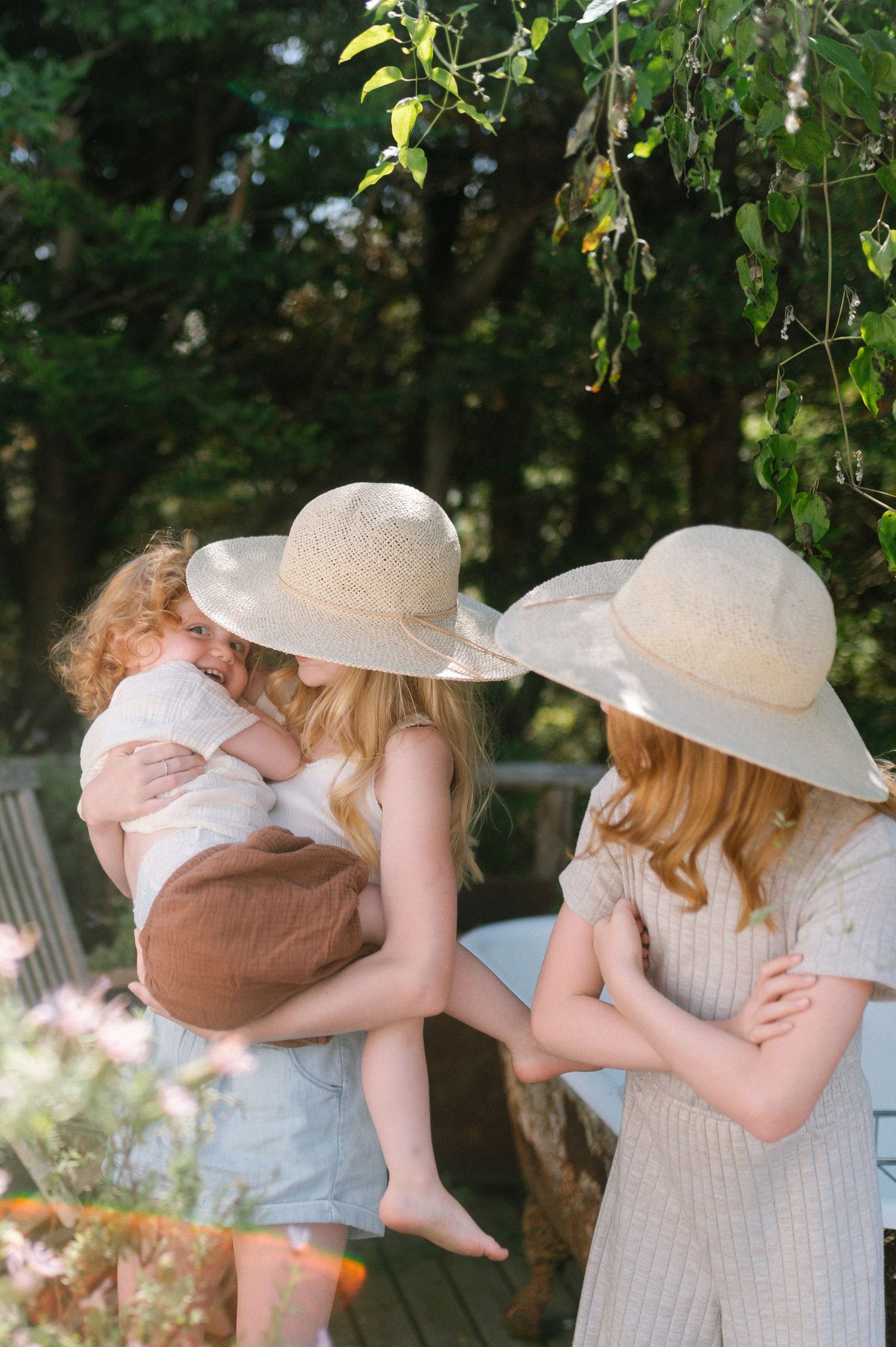 Two people in sun hats share an embrace on a sunny garden porch.