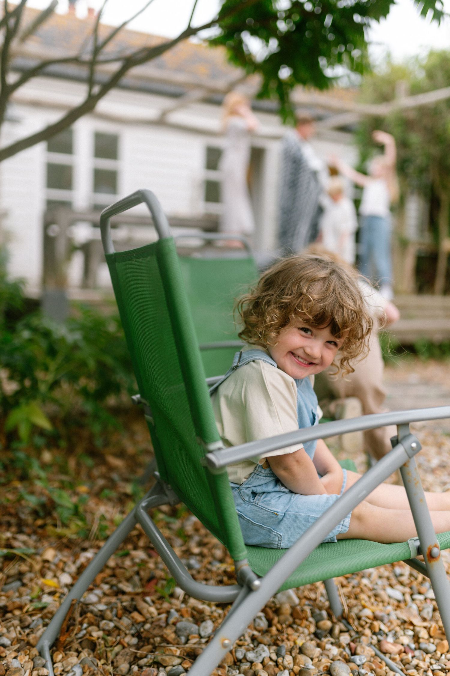 Child lounging in green folding chairs outdoors on a sunny day.