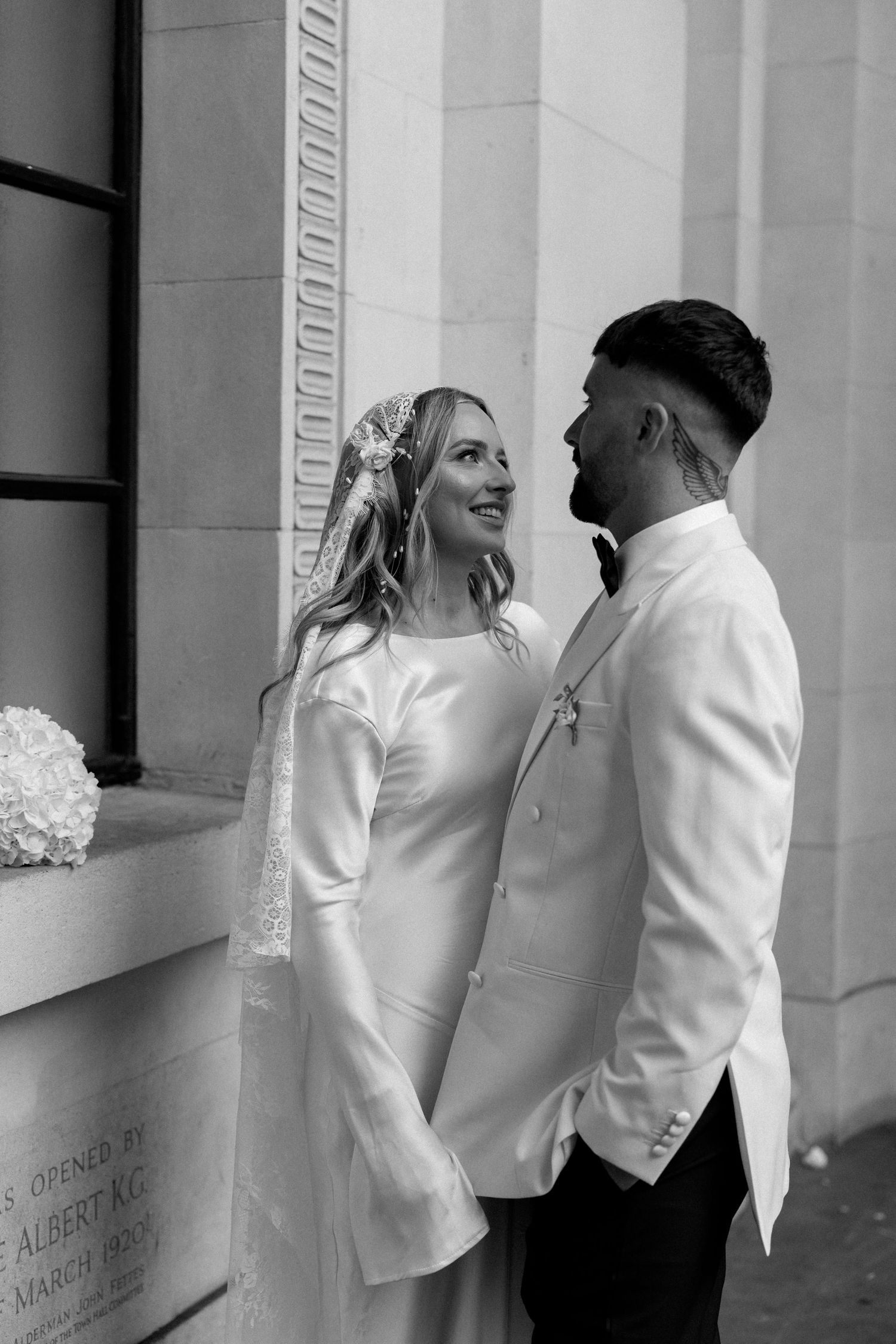Candid black and white photo of wedding couple laughing together by stone column.