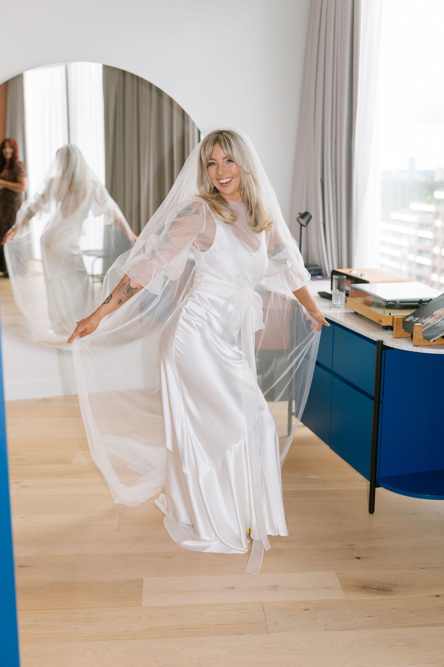 A person in a flowing white dress twirls gracefully in a bright modern room with wooden floors.