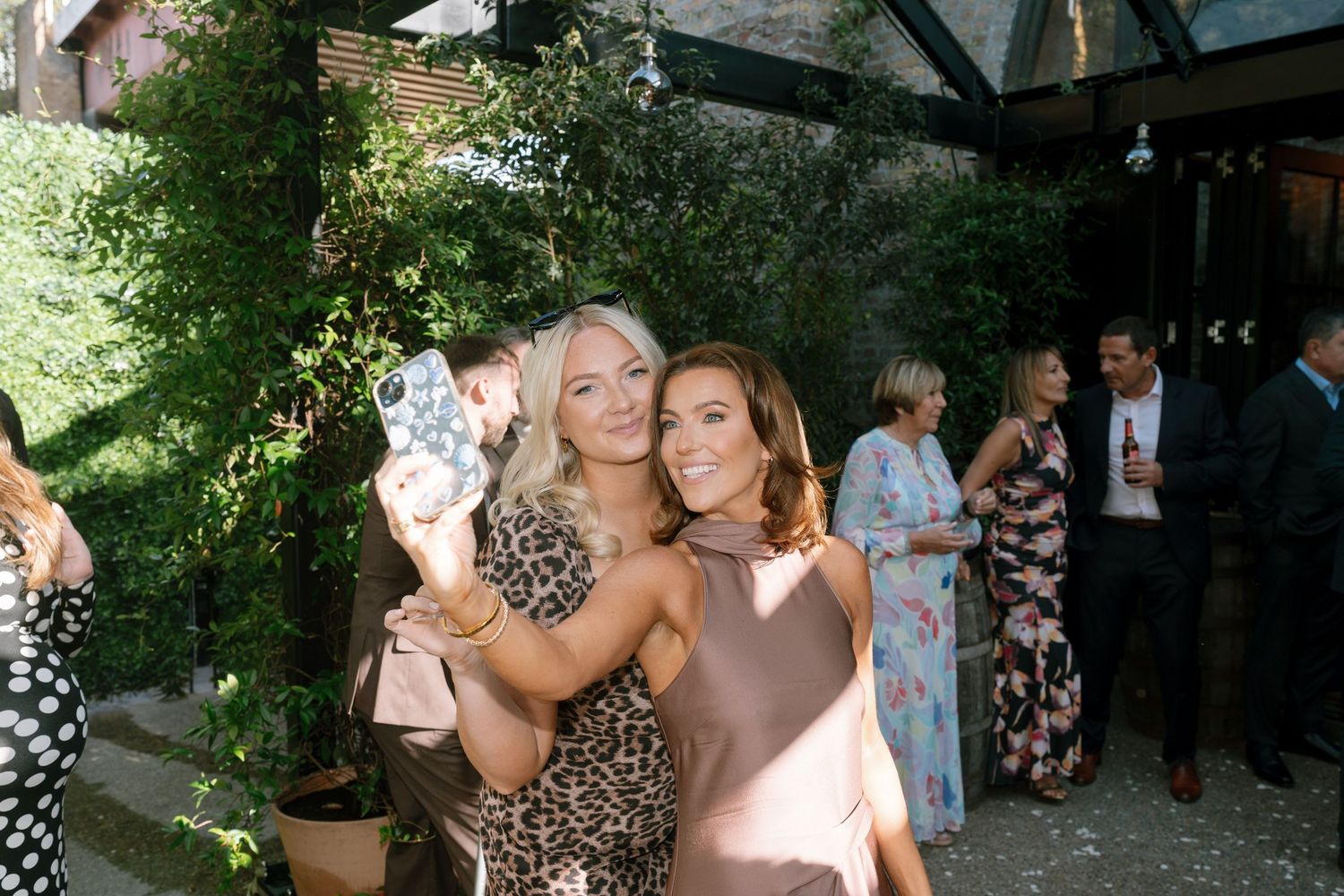 Wedding guests taking selfie at outdoor garden reception.