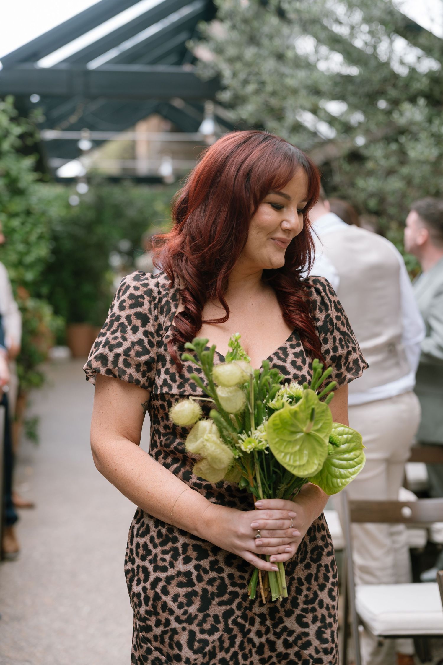 Person in leopard print dress holding green and white floral bouquet at outdoor event.