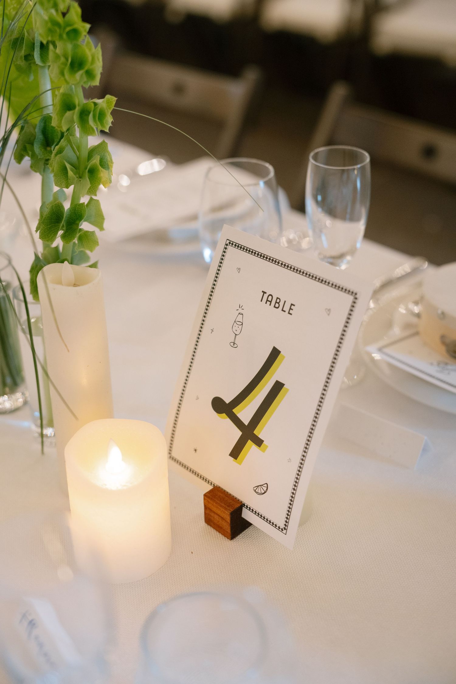 Minimalist table numbers and candle centerpieces on white tablecloths at wedding reception.