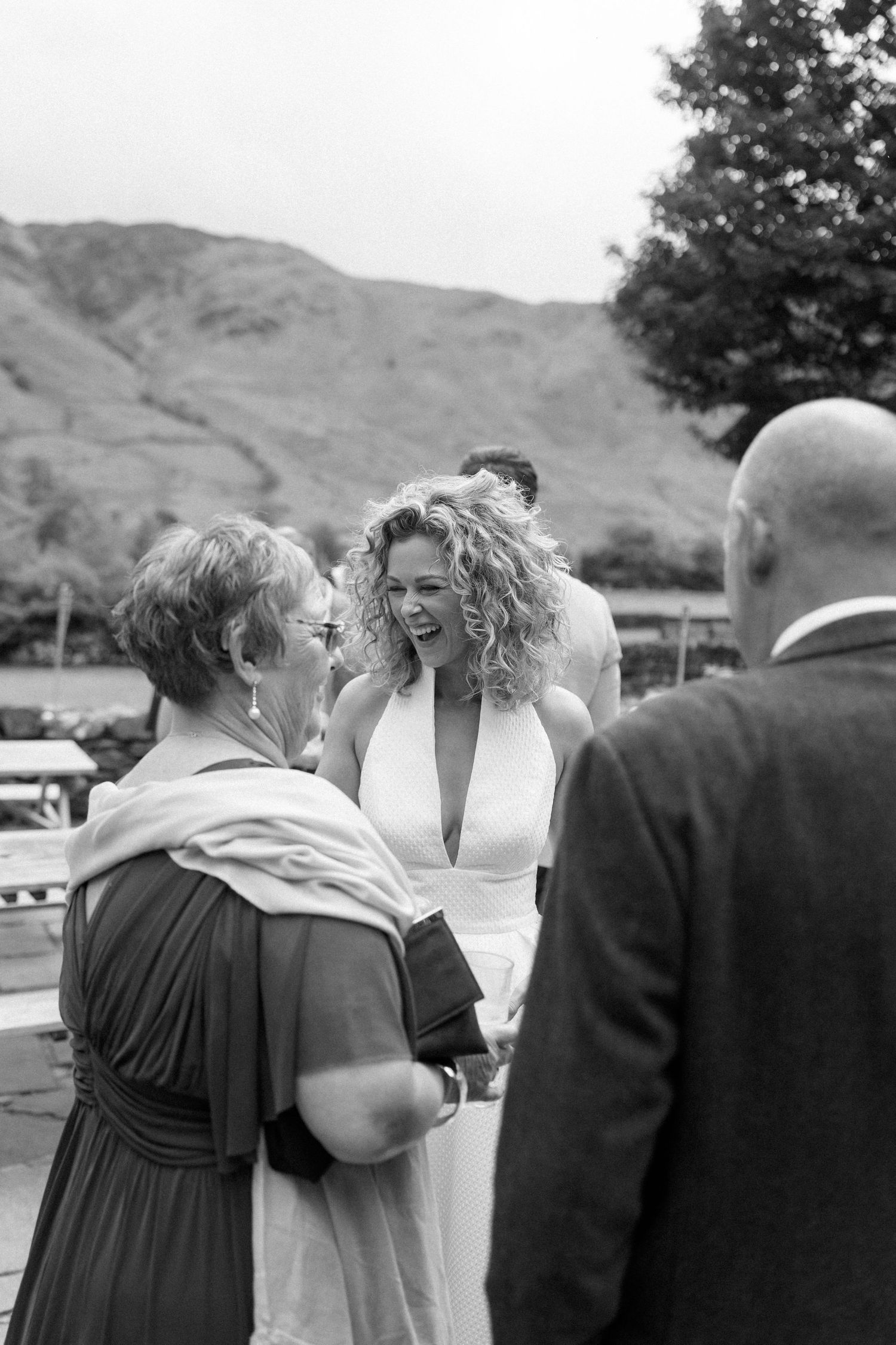A group of people gather outdoors for a celebratory moment with rolling hills visible in the background.