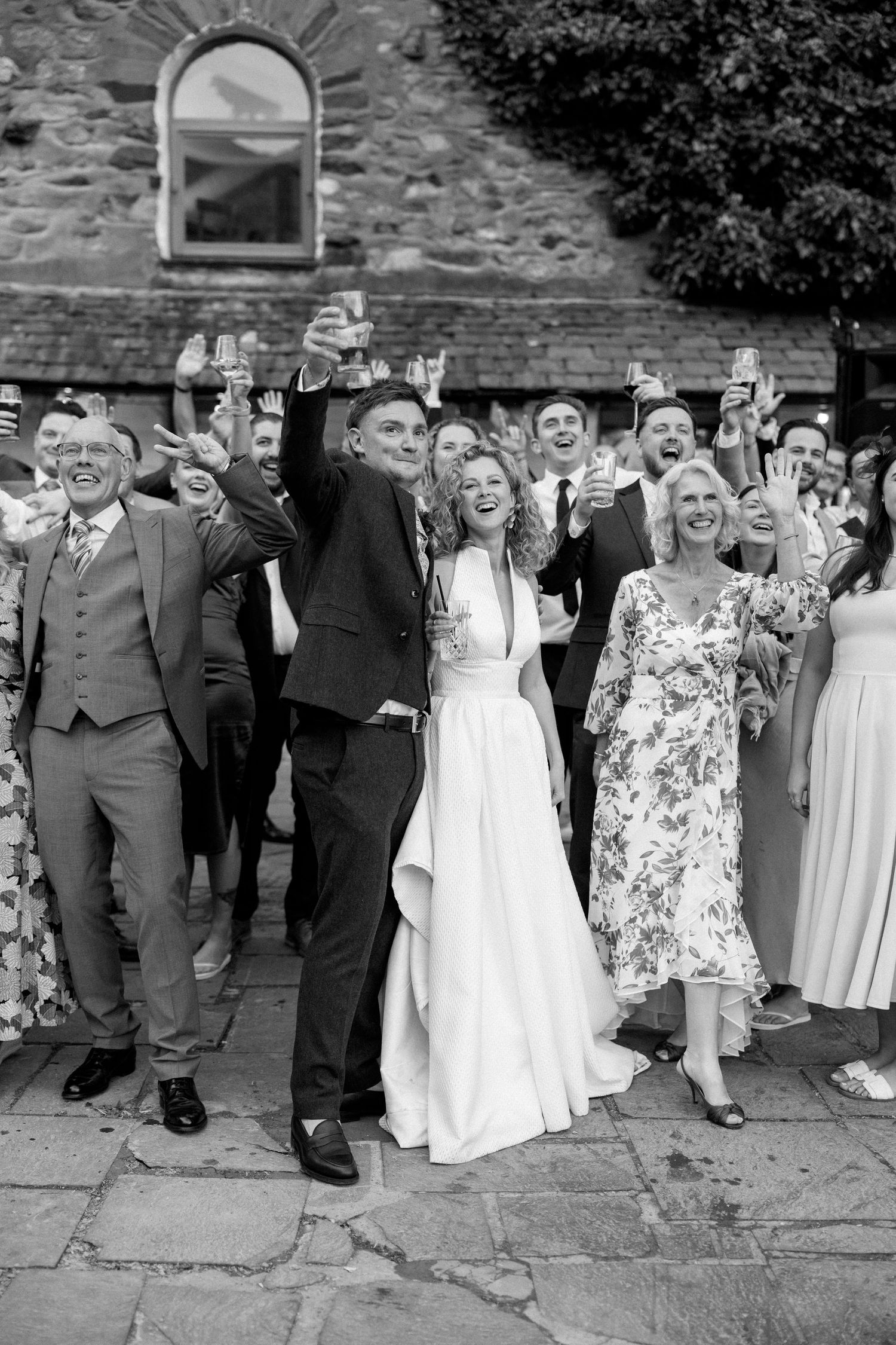 Wedding party poses against stone wall during outdoor celebration.
