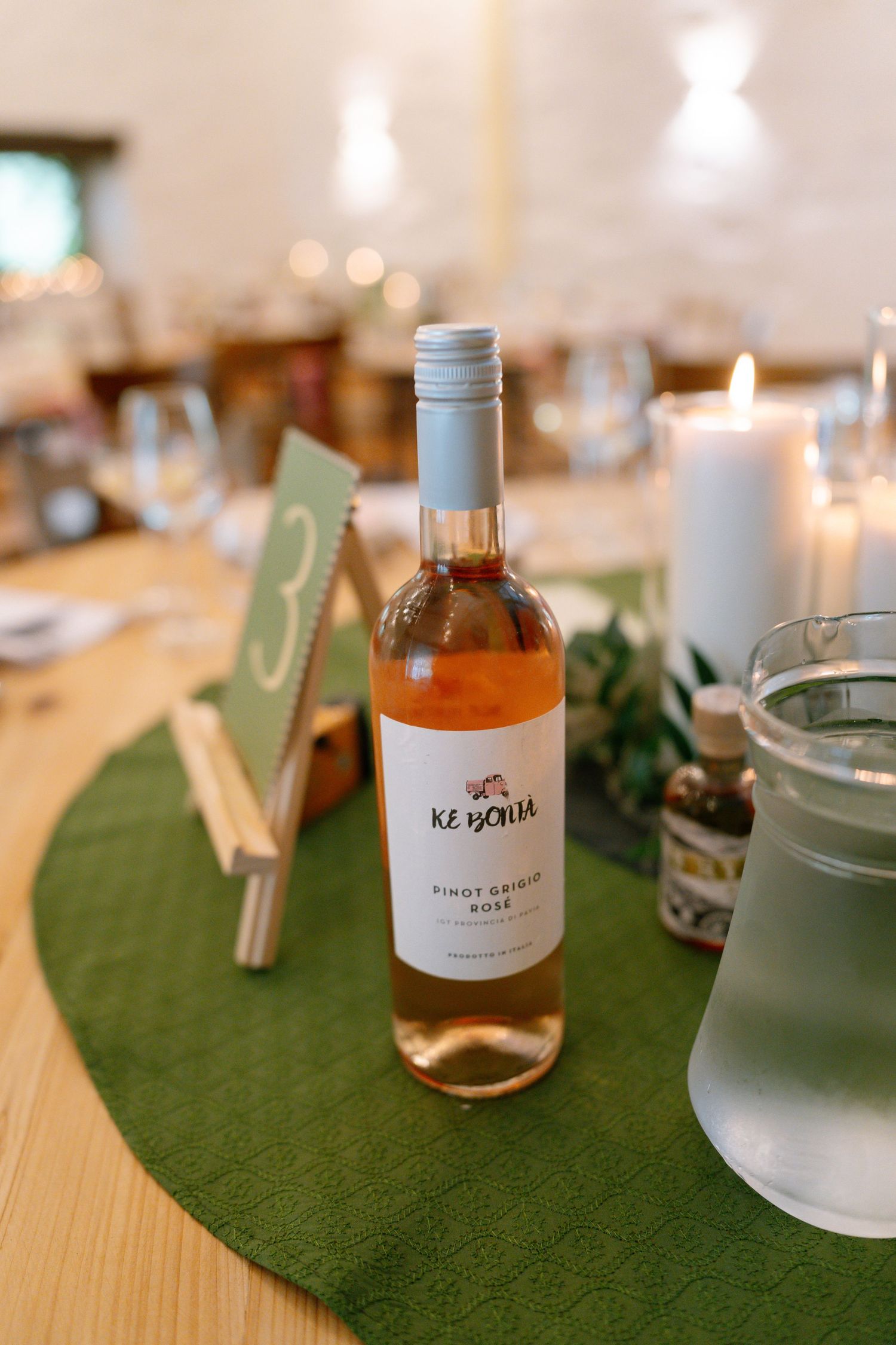 Wedding reception table decor with candles and bottles on green moss runners.