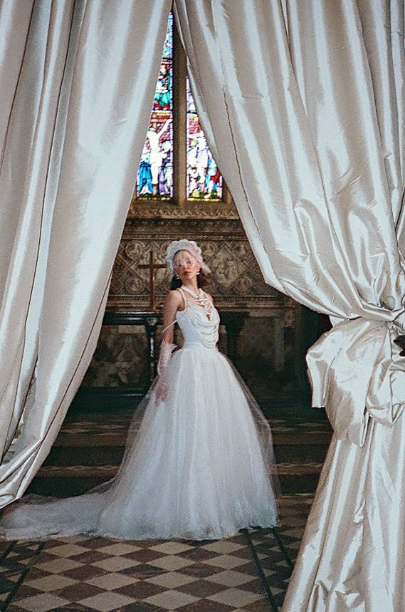 Bride in flowing white wedding gown poses gracefully in historic church interior with stained glass windows and checkered floor.