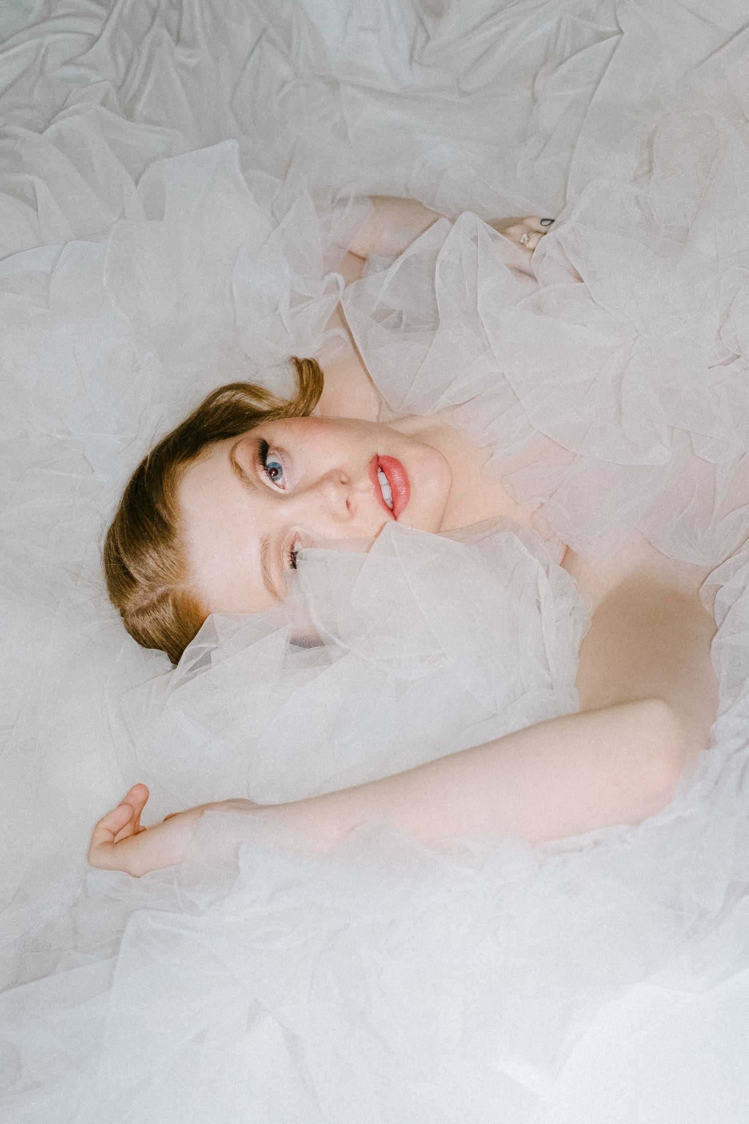 Ethereal artistic portrait series showing delicate poses against soft white tulle fabric in dreamy lighting.