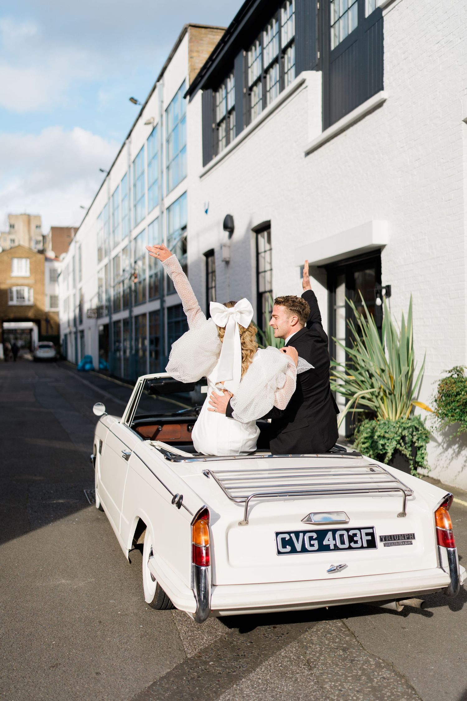 Celebratory moment in white vintage convertible car against modern building backdrop.