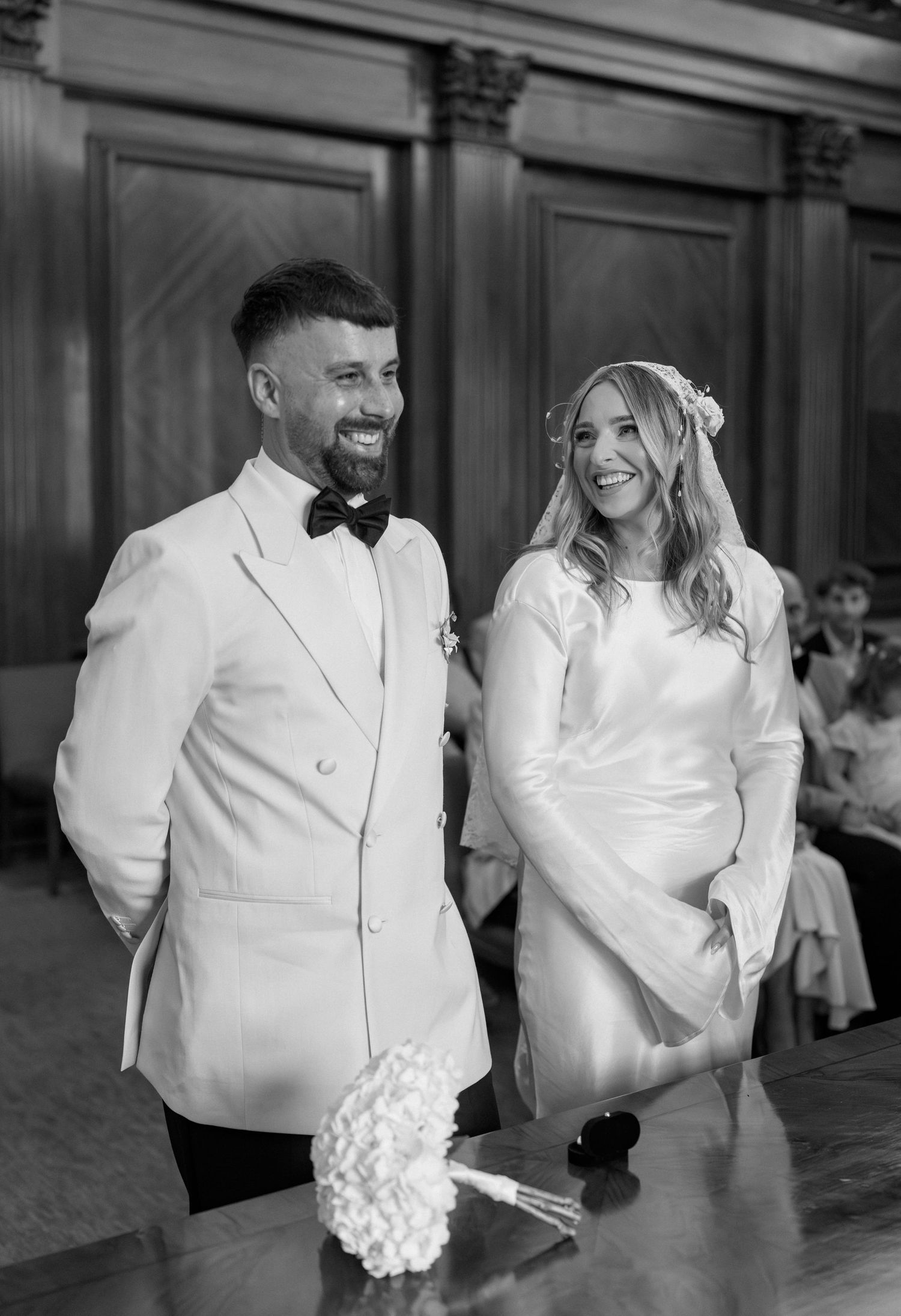 Black and white photo of newlyweds in matching white attire at their civil ceremony.