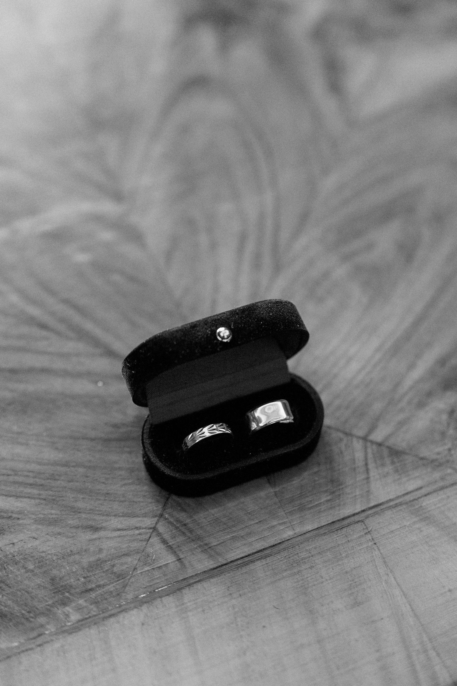 Wedding rings nestled in a black velvet box on a wooden surface.