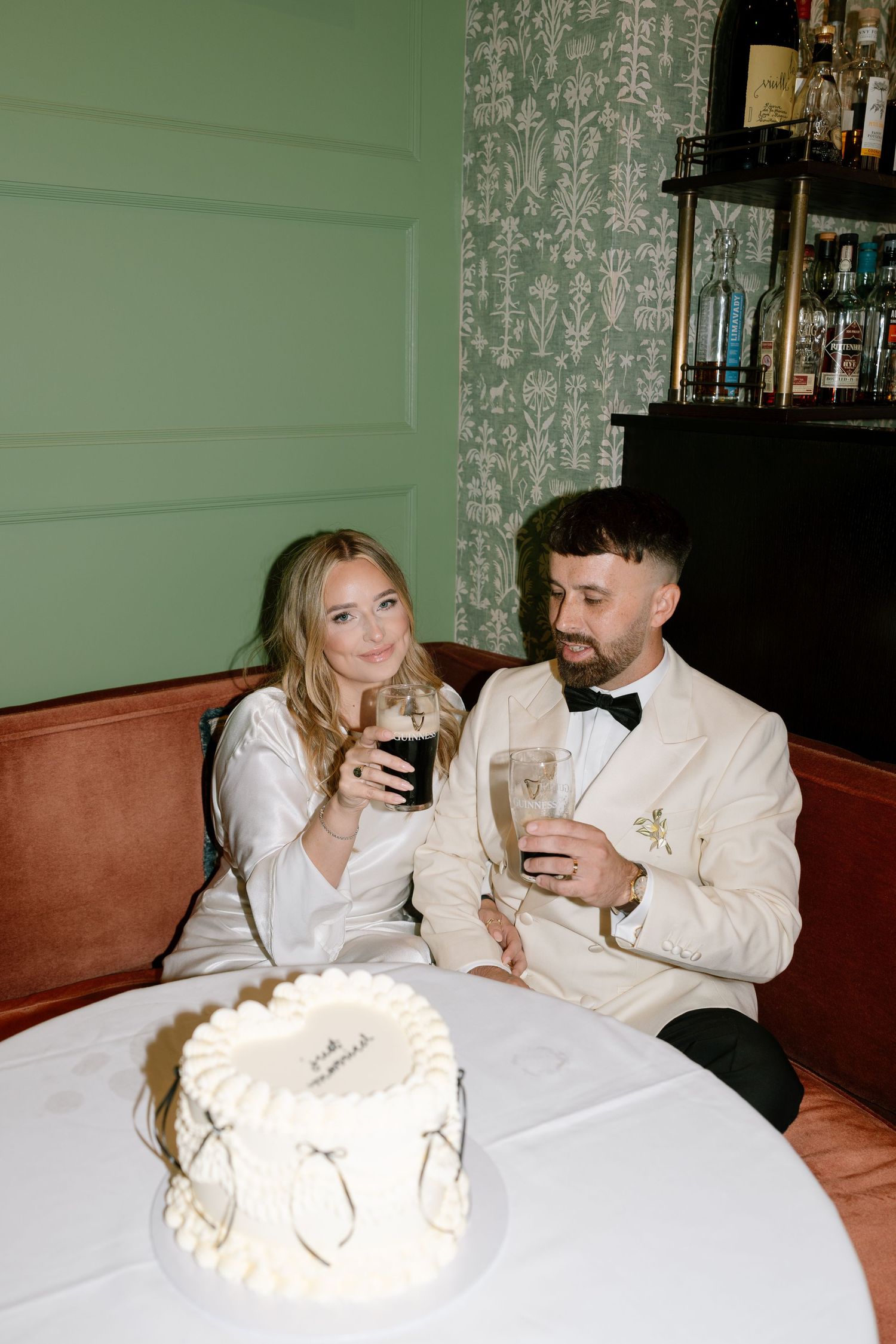 A couple toasts with drinks at a table with wedding cake.