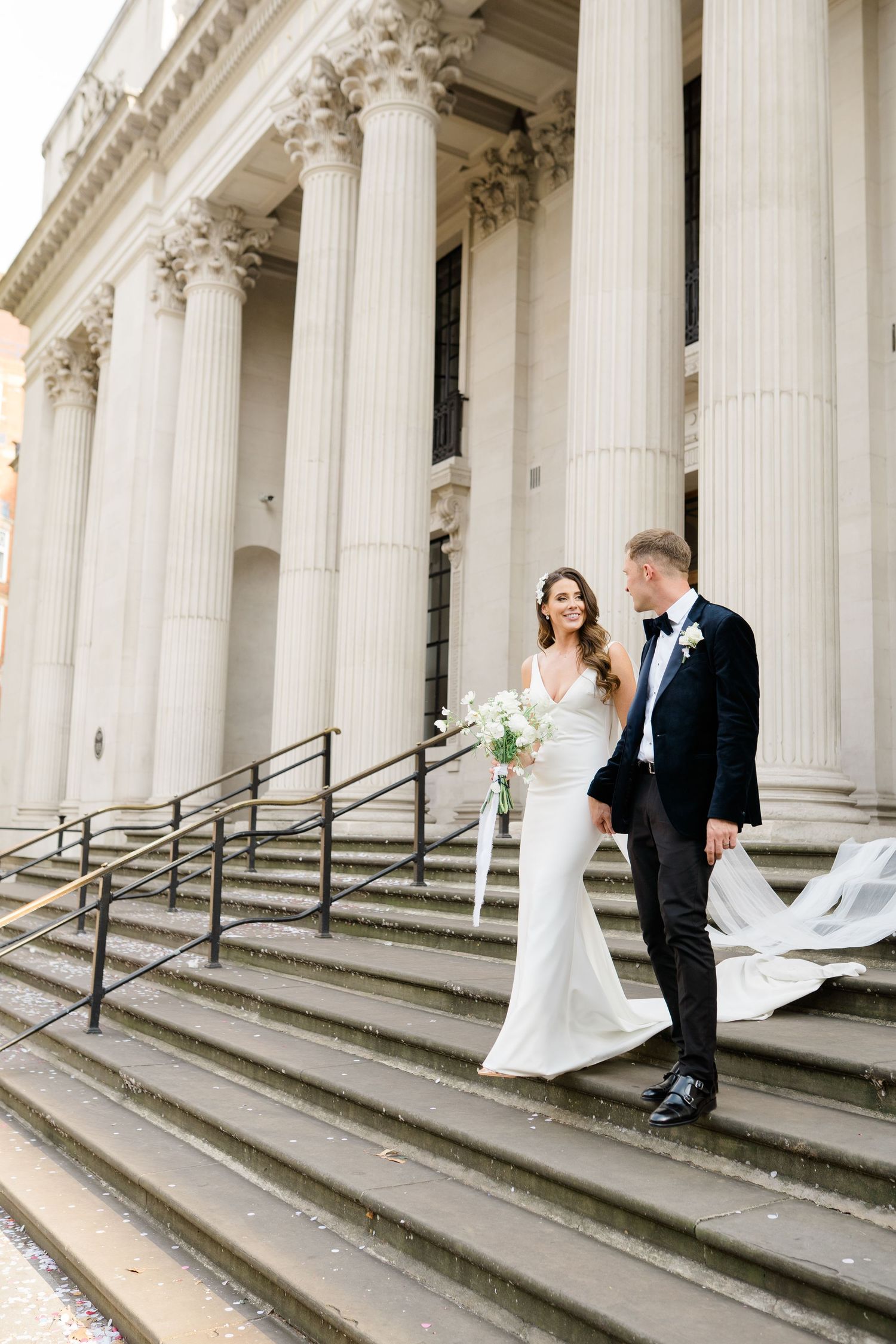 Wedding couple poses on grand stone steps with classical columns.