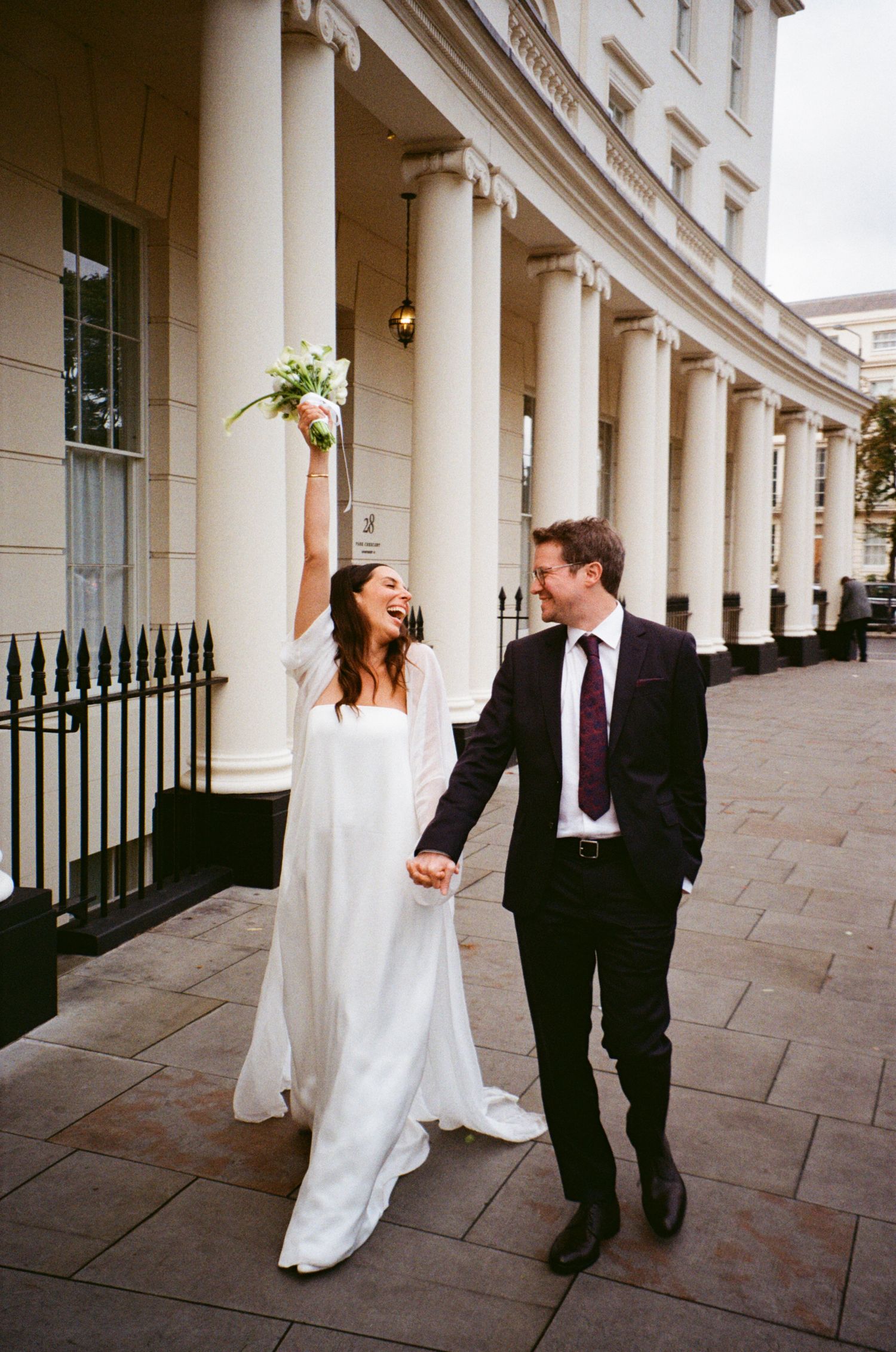 A couple shares a joyful moment under a curved colonnade with classic white columns.