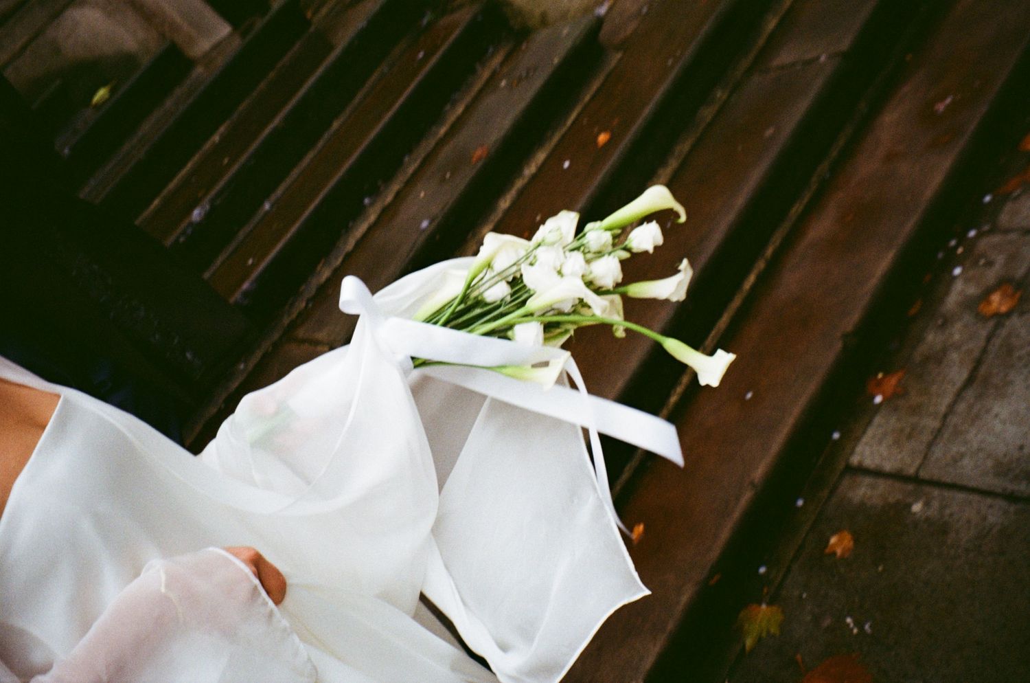 Wedding bouquet with white flowers and ribbons arranged on a dark wooden surface.