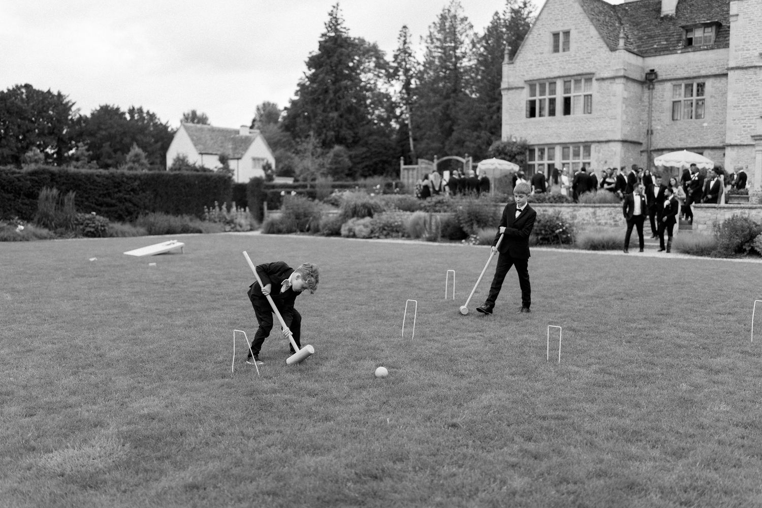 Black and white photo of wedding guests playing croquet on a lawn outside a manor house.