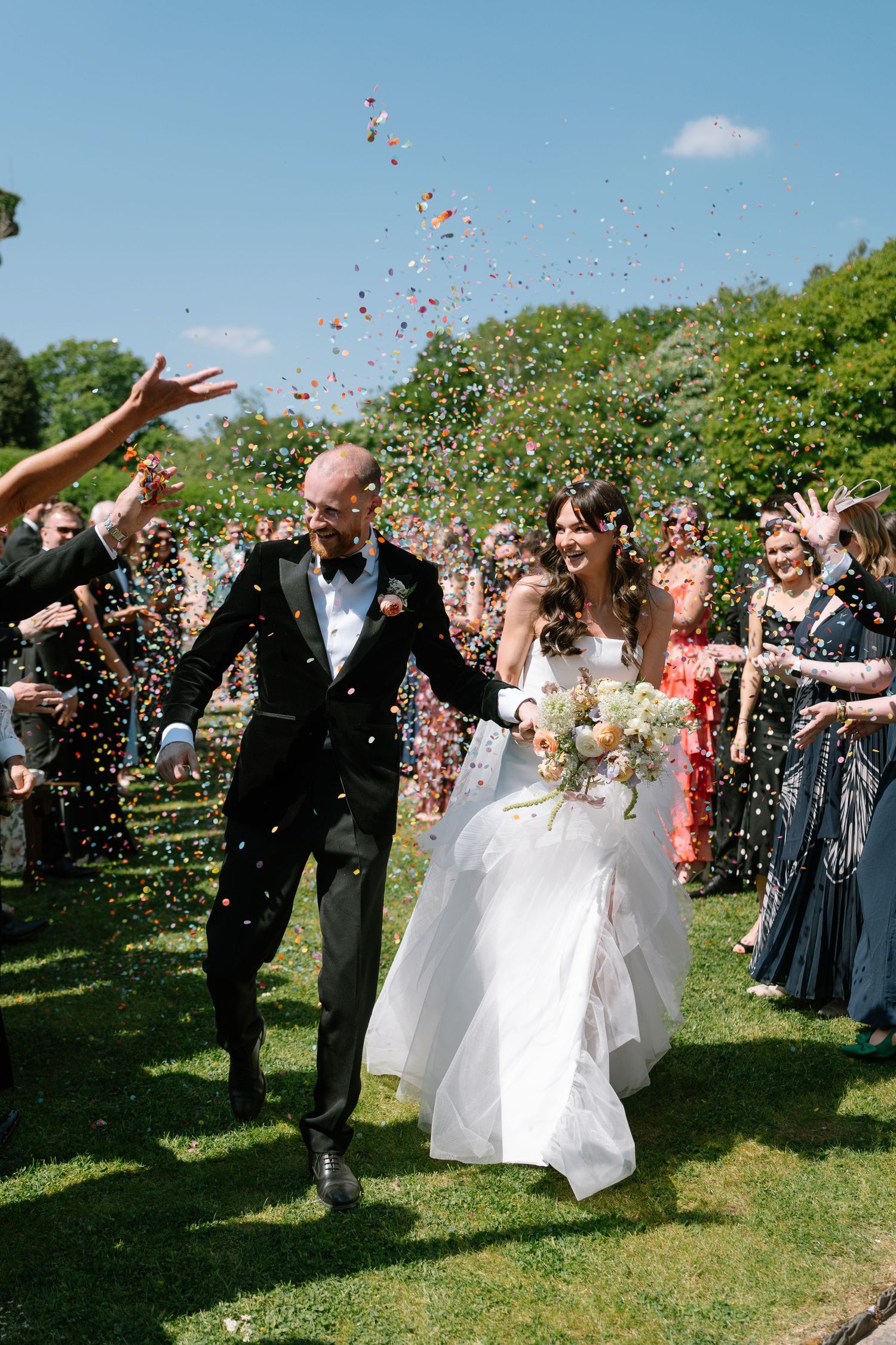 Wedding party and guests create a festive atmosphere with confetti against a blue summer sky.