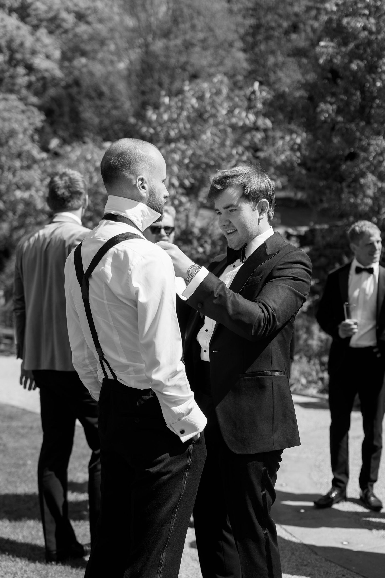 Black and white photo of wedding party members helping with formal attire adjustments.