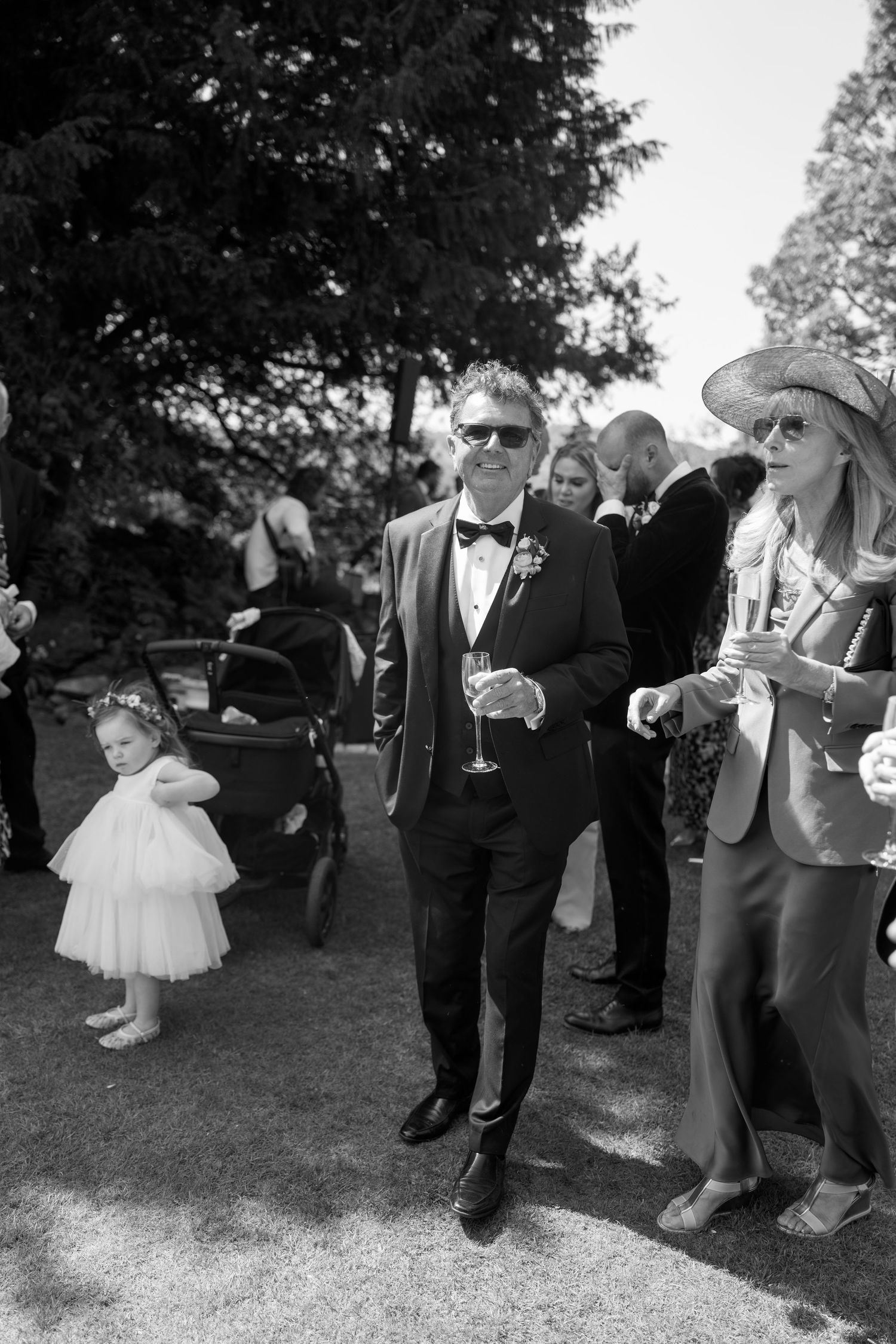 Wedding guests mingle outdoors at an elegant garden reception with a small child in a white dress.