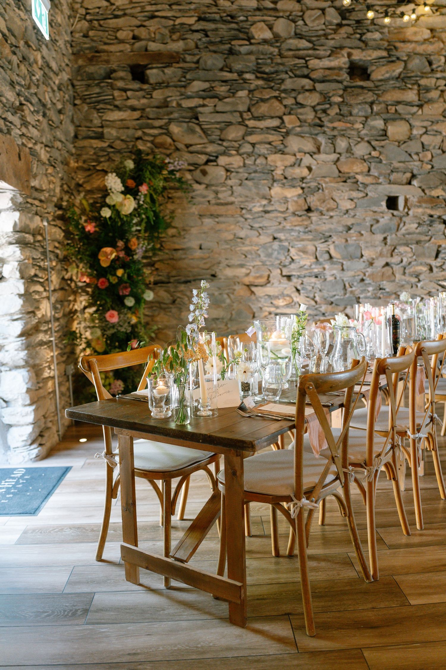 Rustic stone-walled dining room with wooden tables and chairs set for an elegant event.