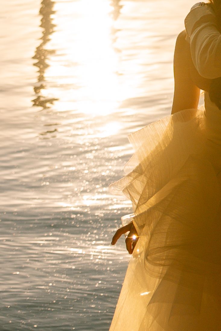 Sunlight sparkles on lake water creating a golden glow through flowing white fabric.