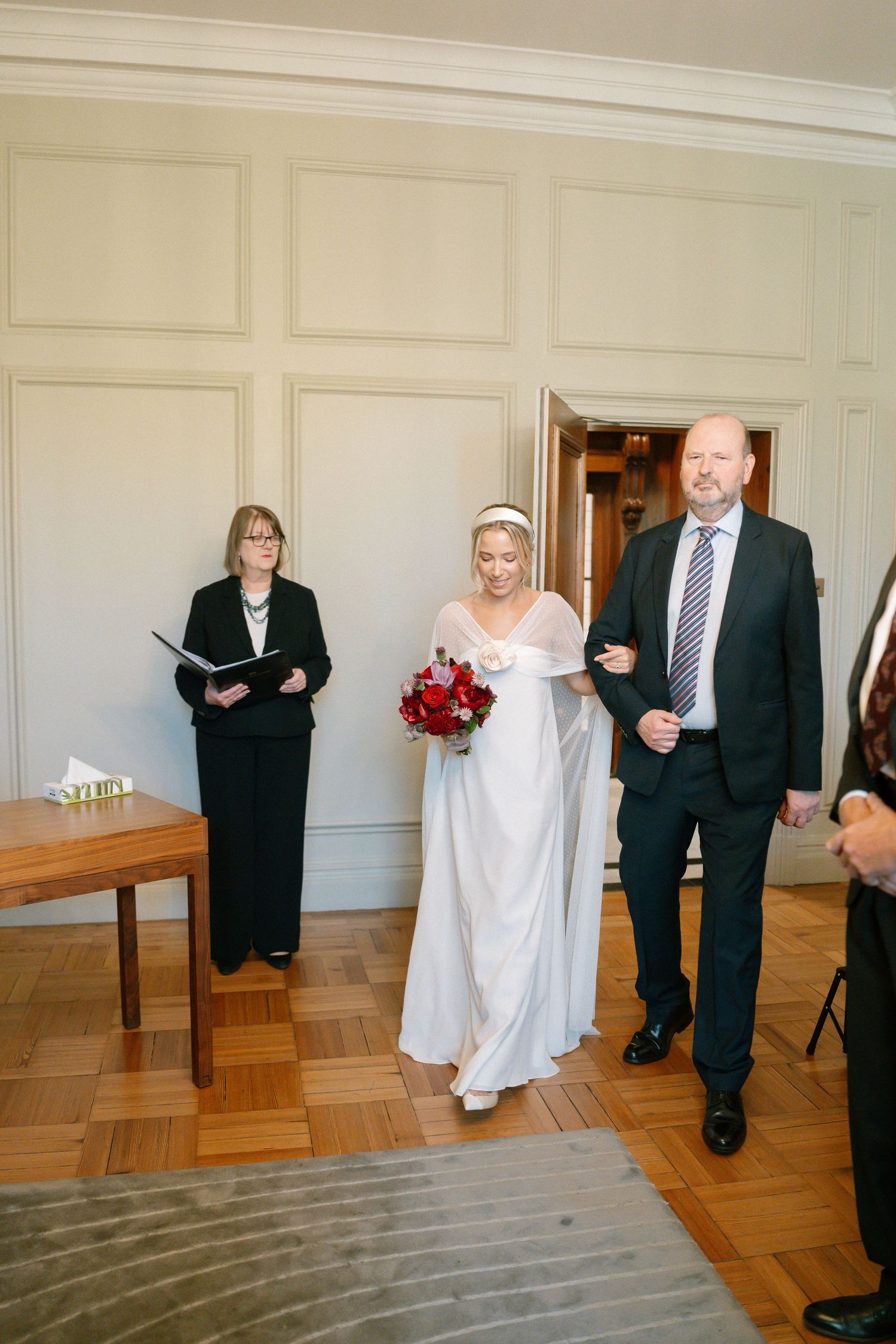 Wedding ceremony scene in elegant room with paneled walls and hardwood floors.