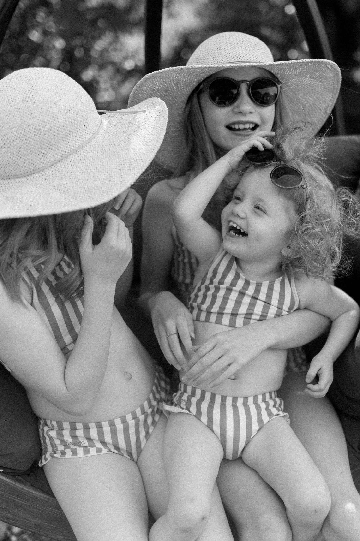 Children in striped swimsuits laughing together under sun hats.