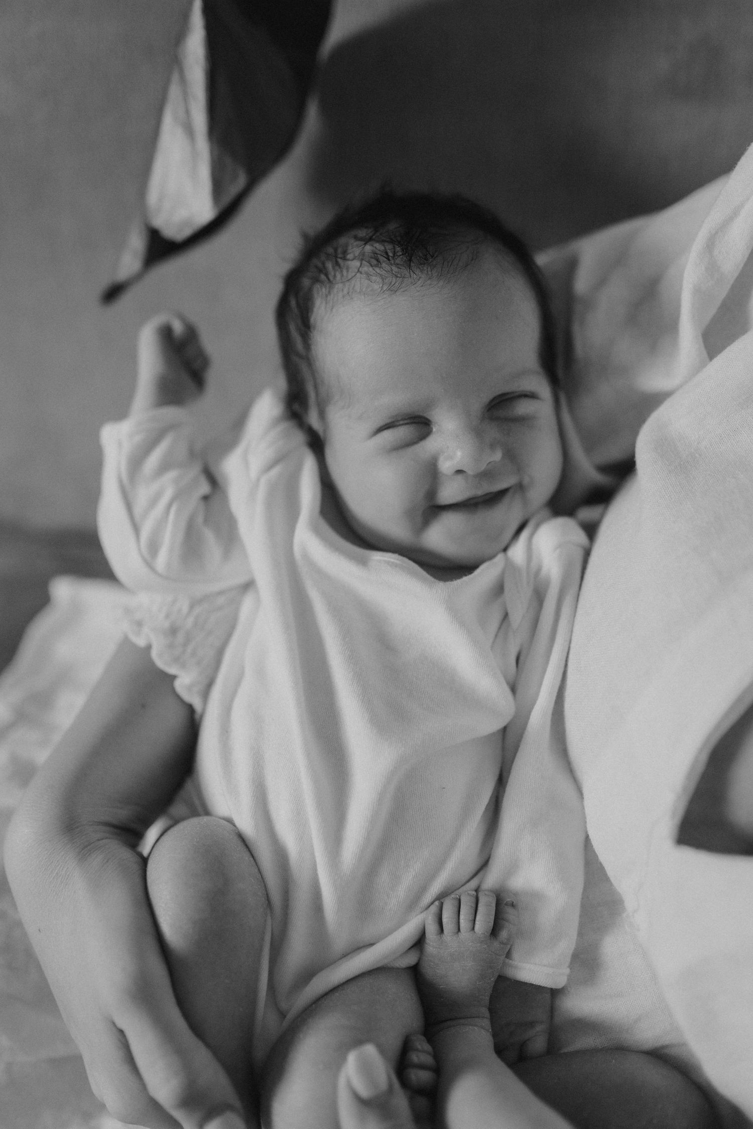 A smiling infant in white clothing lying contentedly on soft bedding.