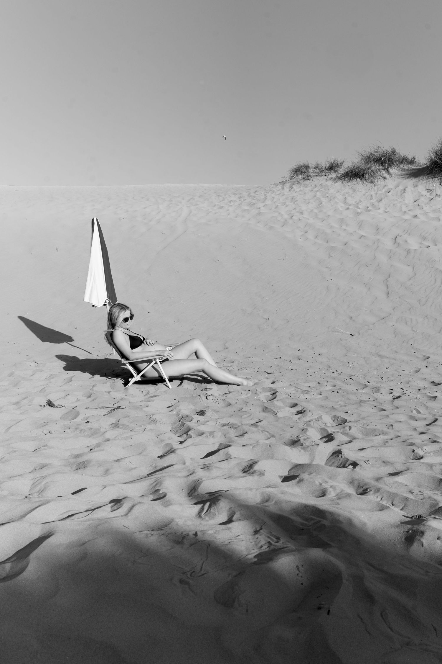 Black and white photograph of an umbrella lying on rippled sand dunes at the beach.