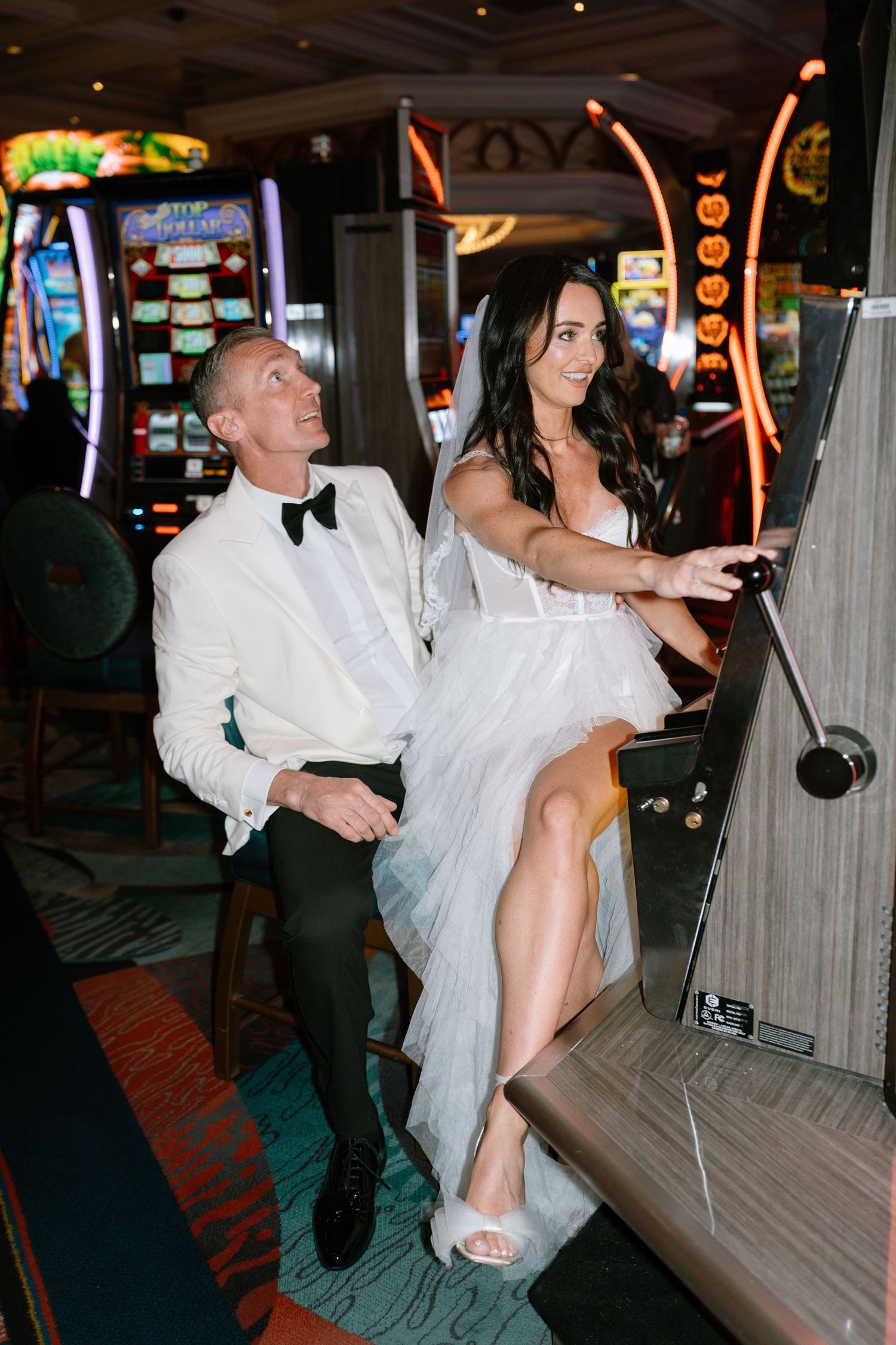 Newlyweds pose playfully among bright casino slot machines.