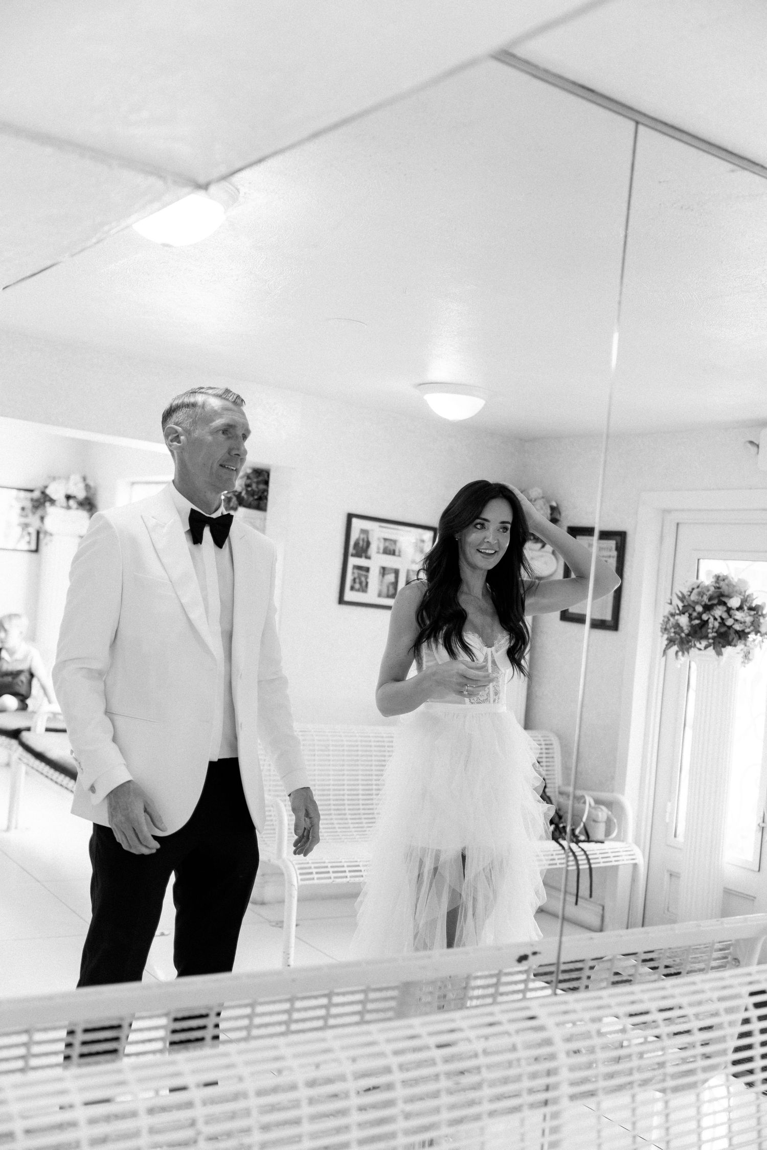Couple takes photos in white chapel interior with mirrors and bright lighting.