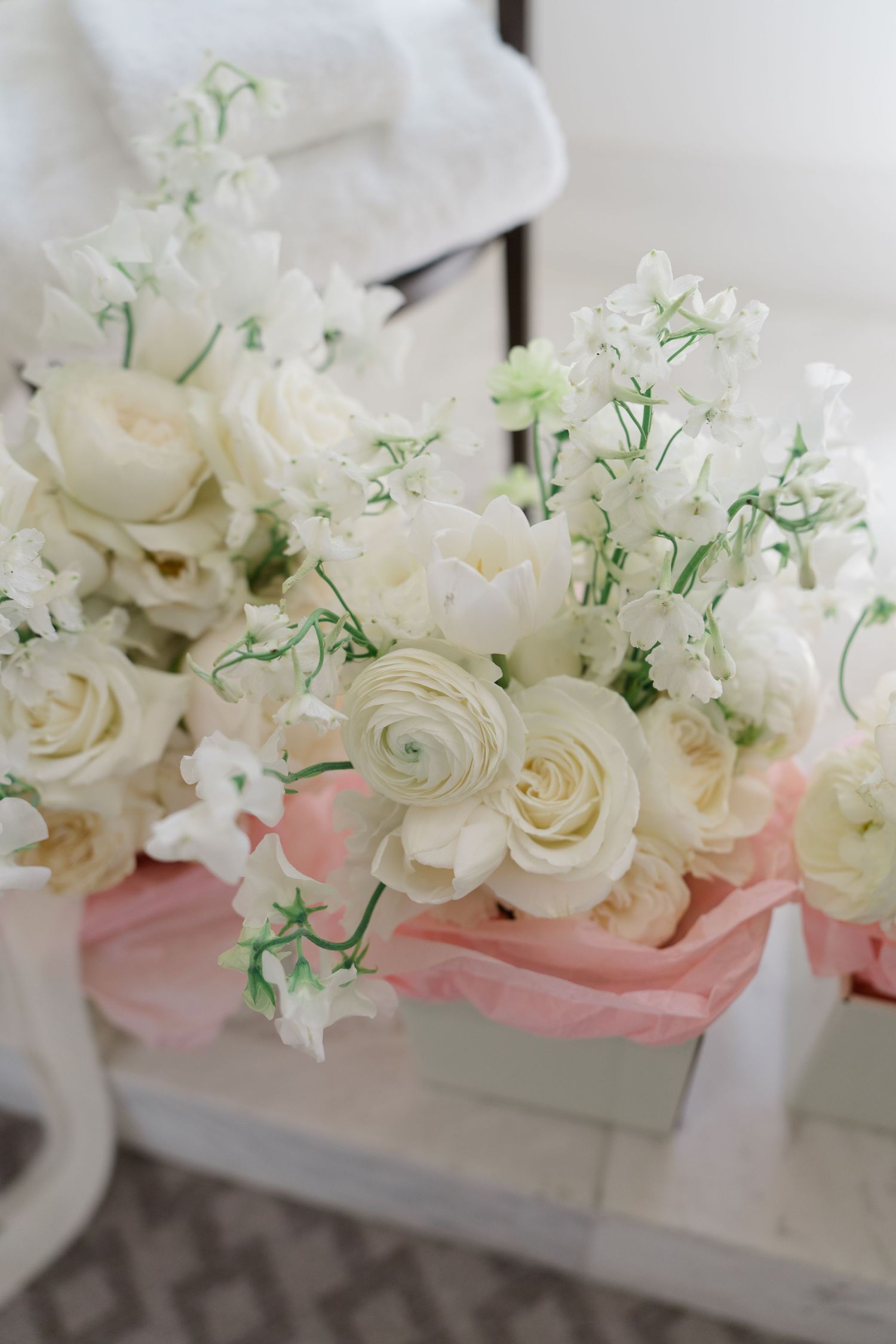 Elegant white wedding bouquet featuring ranunculus, roses, and sweet peas arranged in a soft pink-trimmed white box.