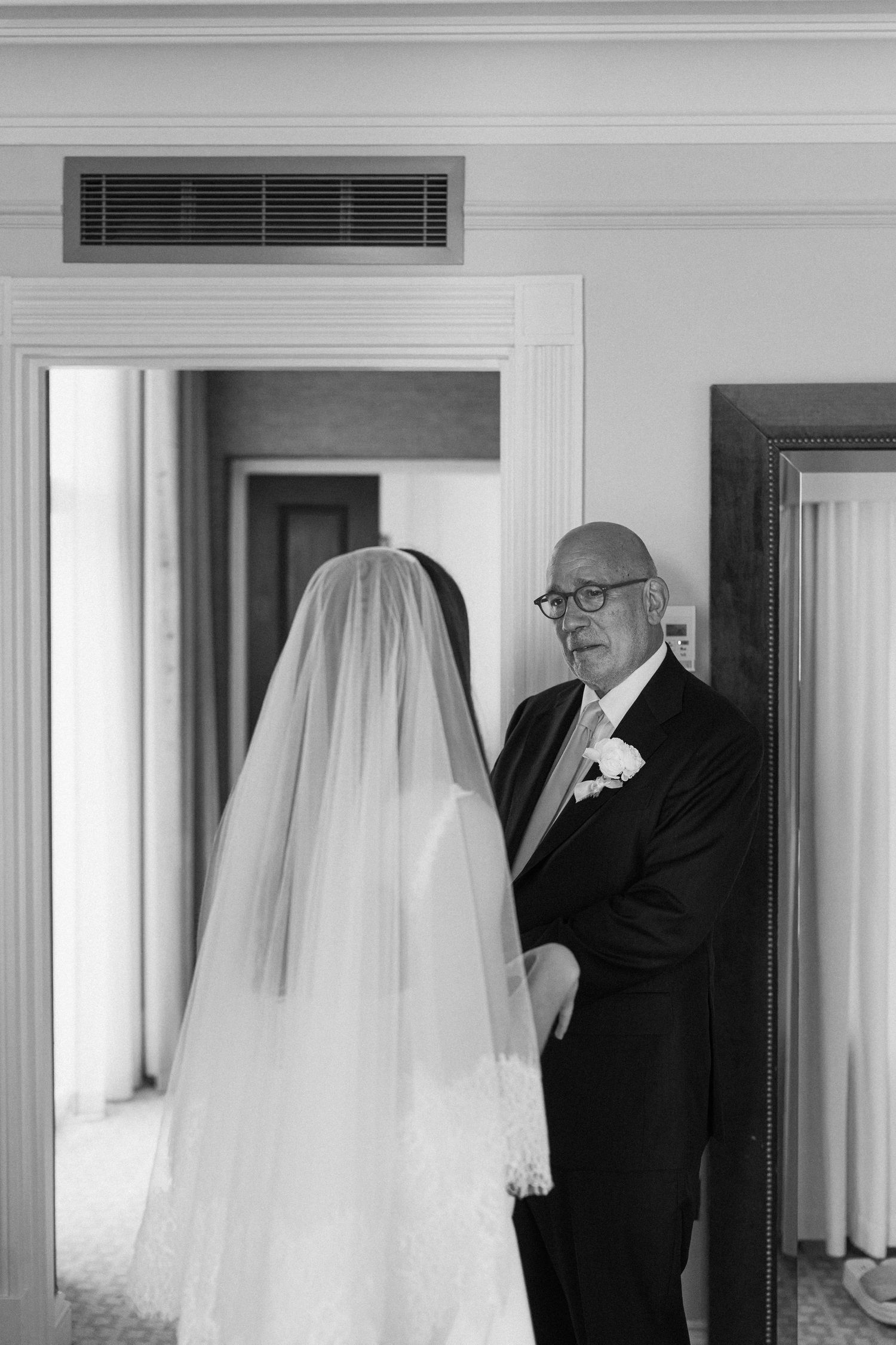 Black and white photo of bride in lace veil sharing emotional first look moment with father.