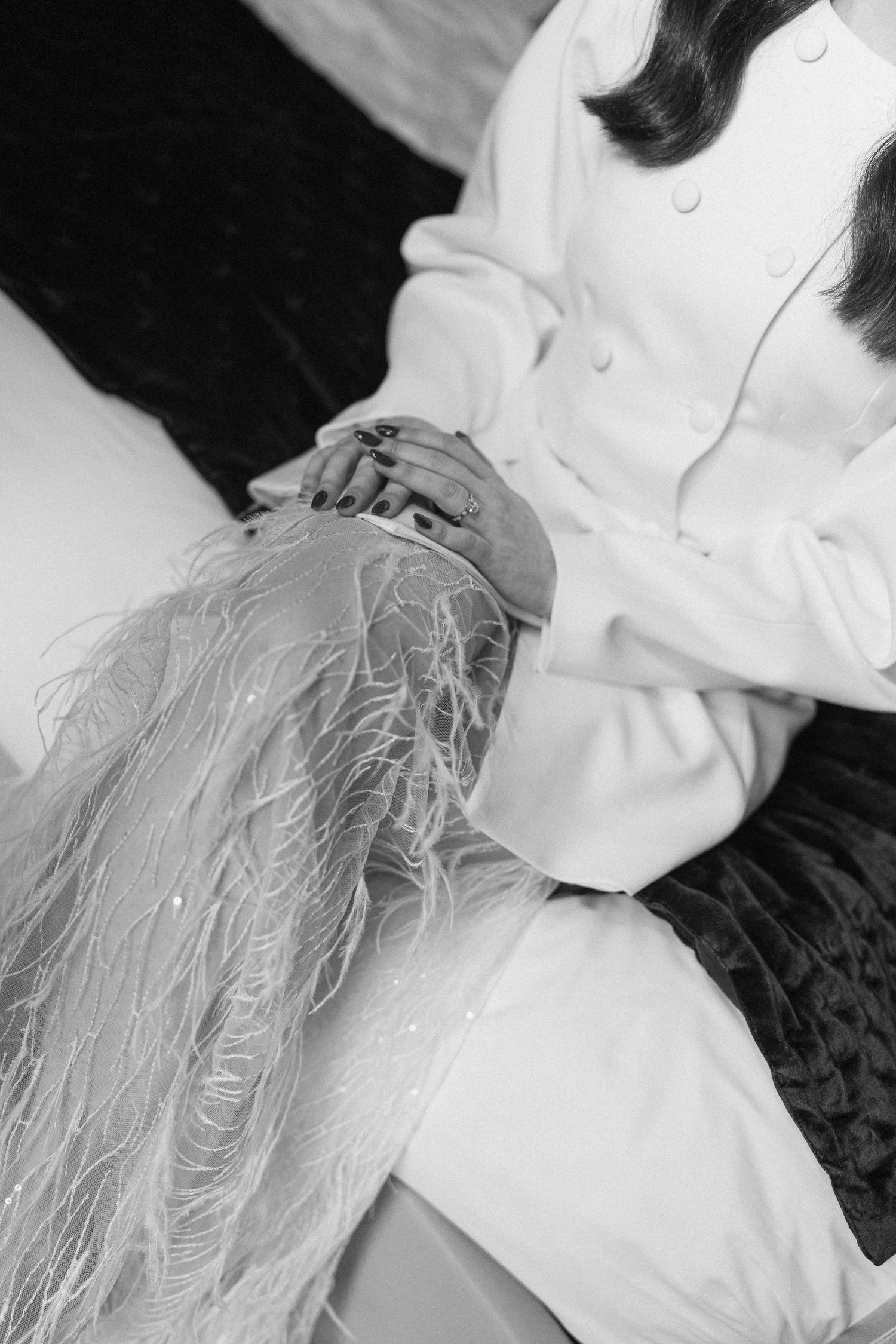 Black and white close-up of bride in feathered wedding dress with hands clasped together.