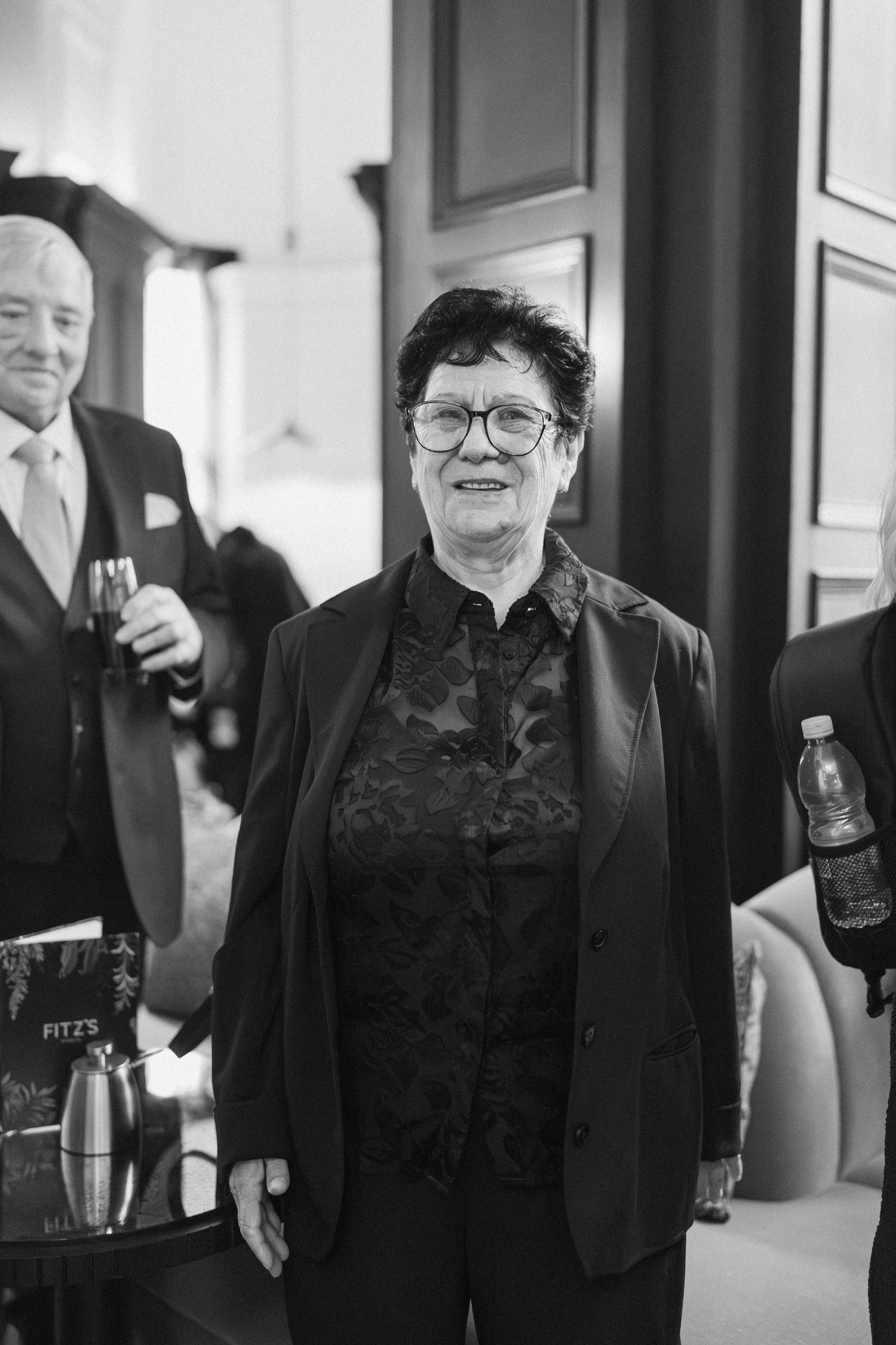 Elegant older woman in black lace blazer smiling at wedding reception in black and white.